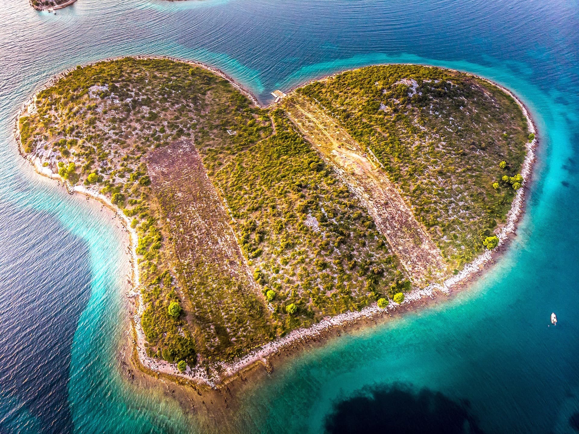 Heart-shaped island with scrubland and paths surrounded by turquoise water, Kornati, Croatia.