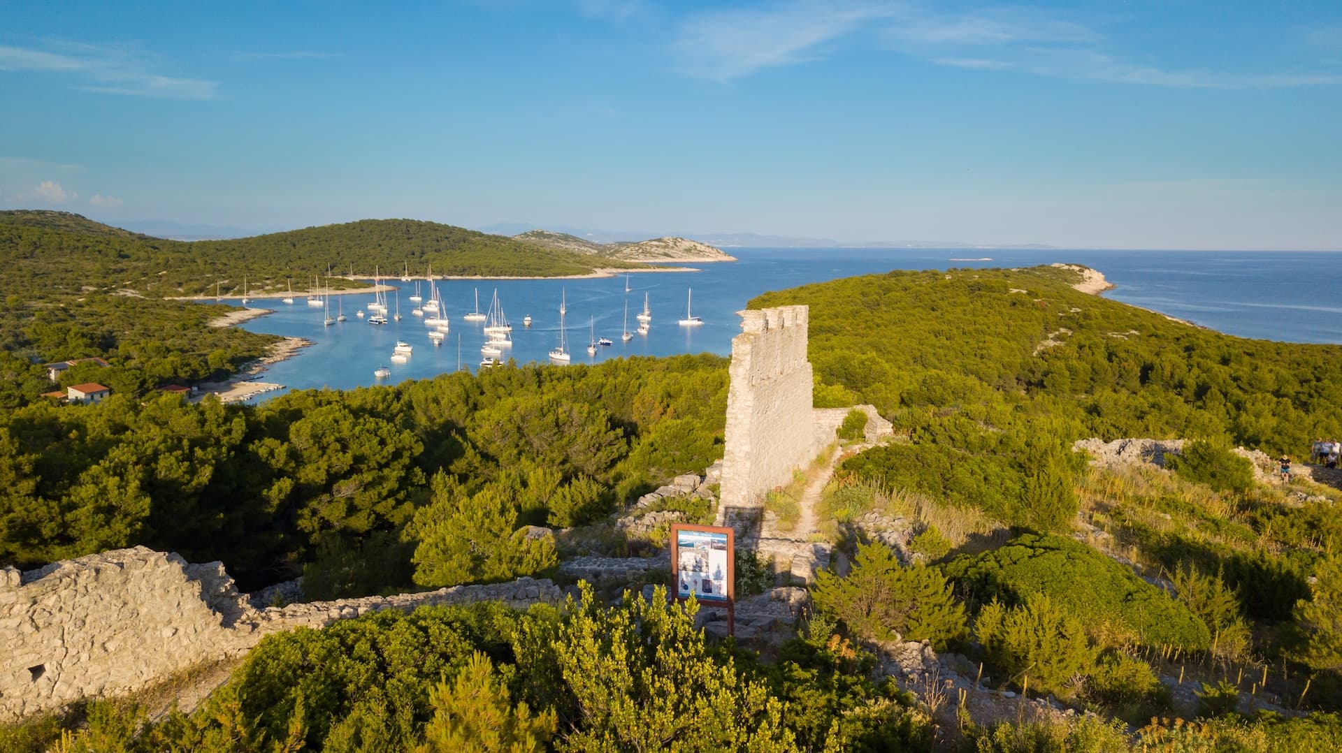 Stone fort ruins overlooking a bay with many sailboats in Zirje Island, Croatia.