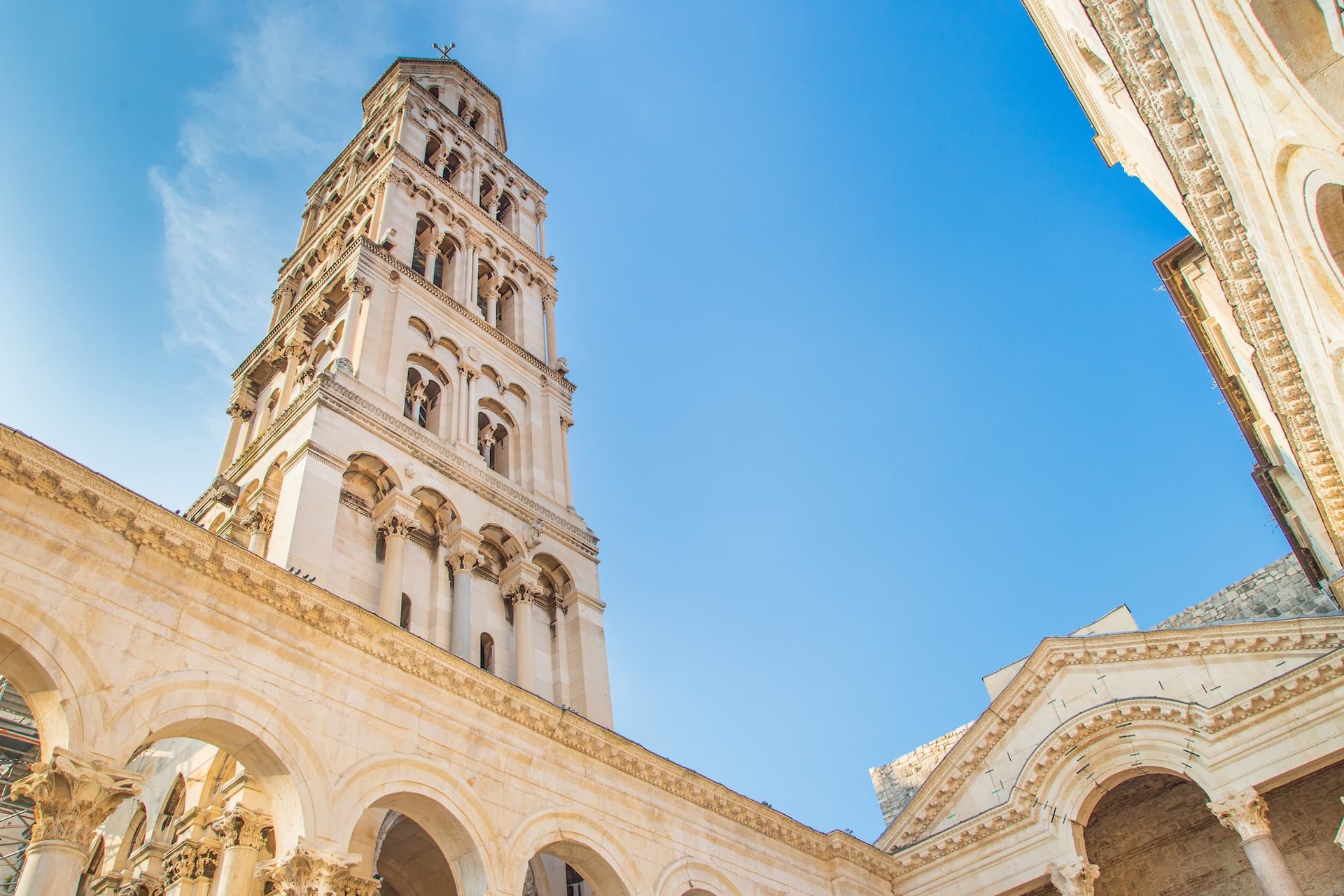 Bell tower and arched stone architecture under a clear blue sky, likely Split, Croatia.