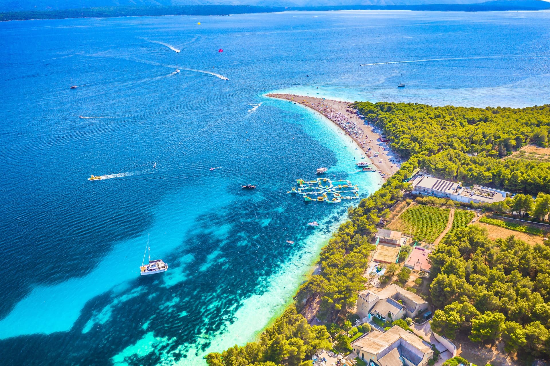 Zlatni Rat beach with turquoise water, boats, and crowded pebble shoreline in Bol, Croatia