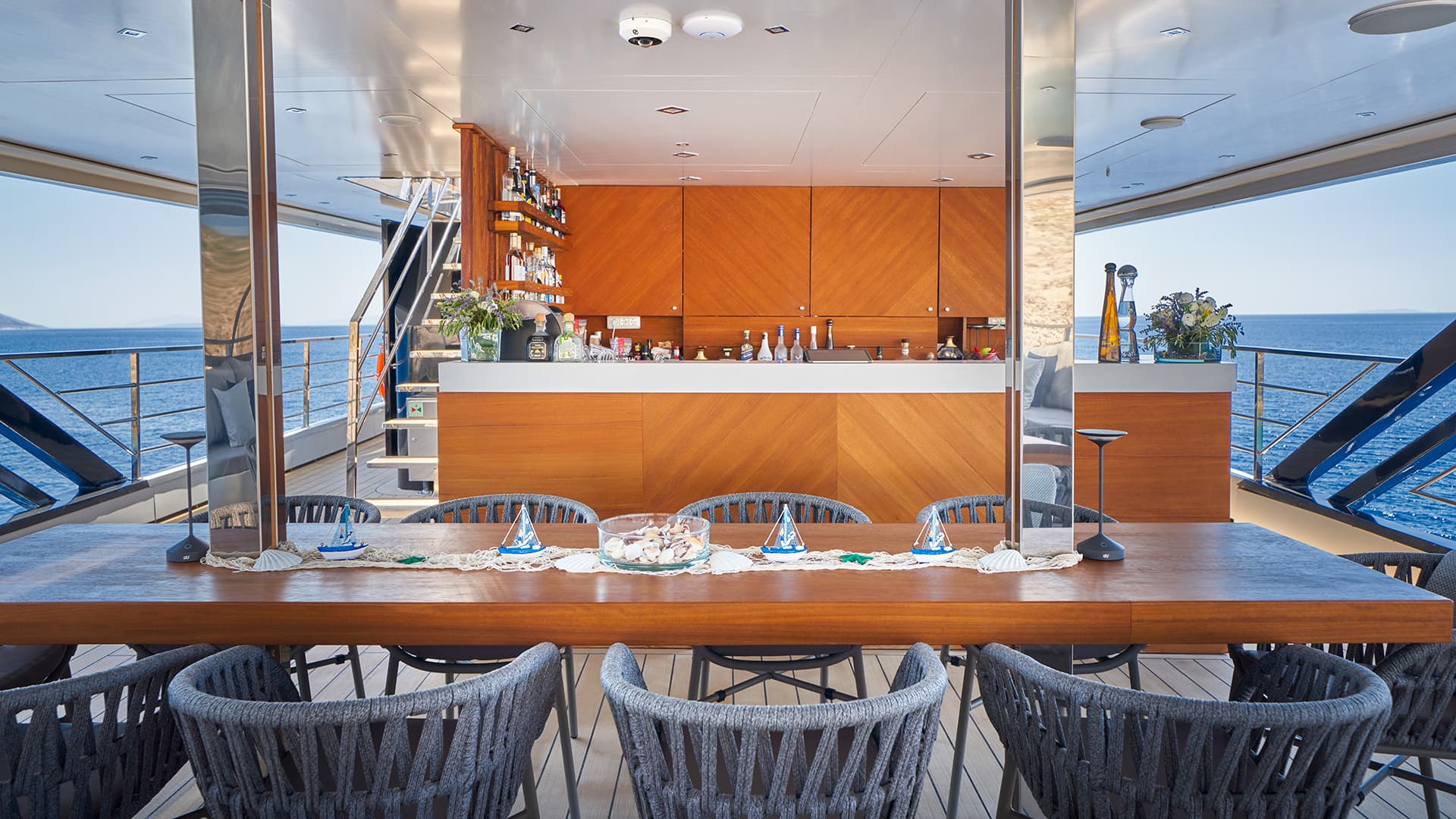 Yacht deck dining area with bar overlooking the blue sea and distant coastline.
