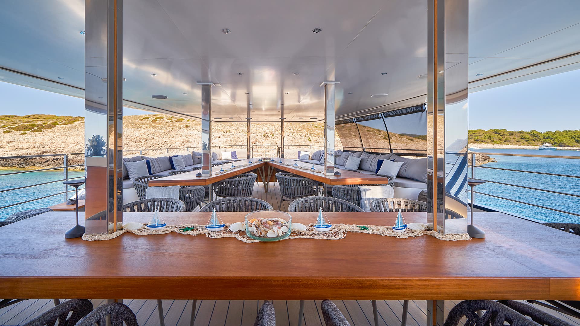 Outdoor dining area on Argo yacht near rocky coastline and blue sea
