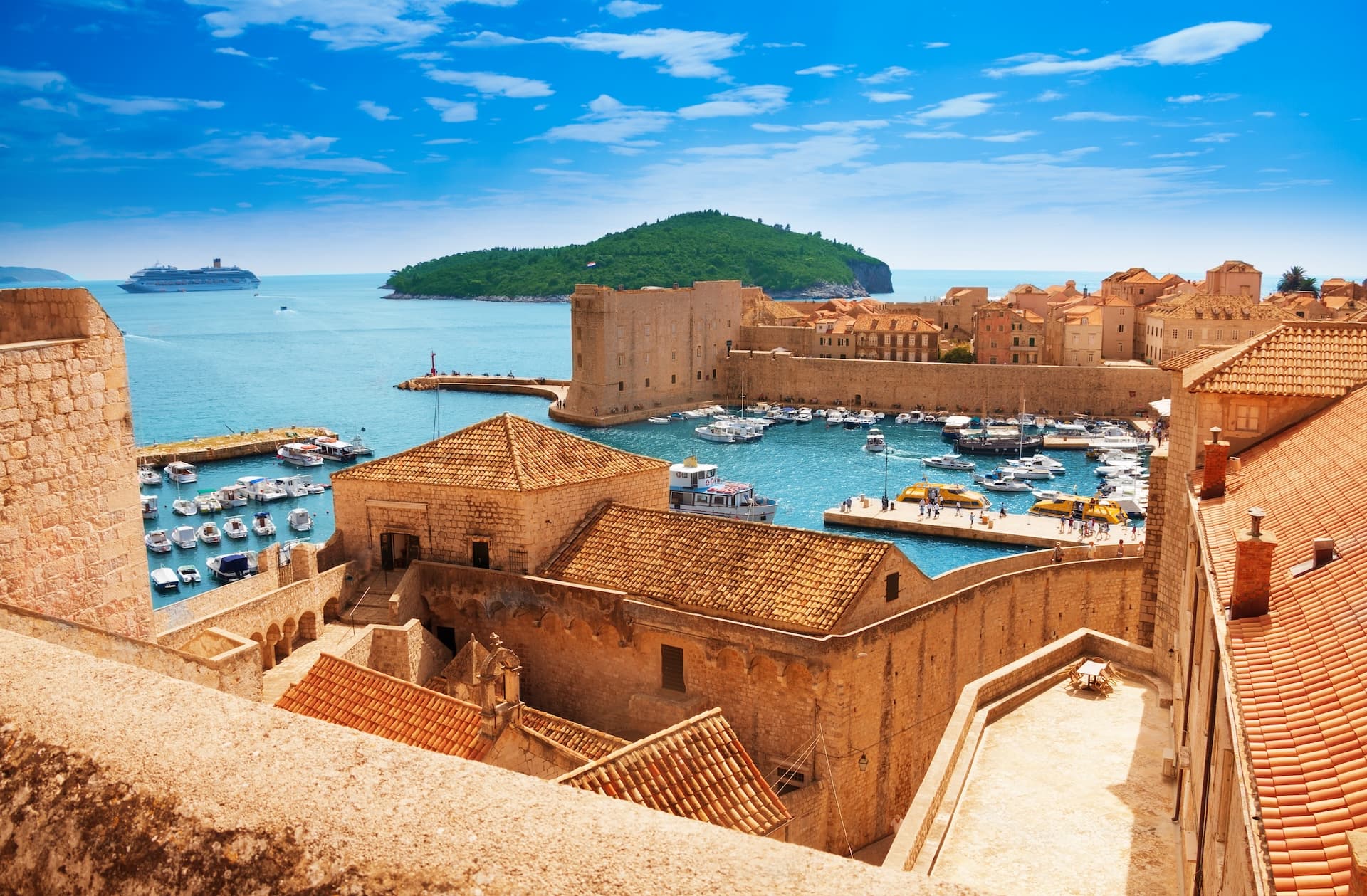 Dubrovnik harbor with stone walls, terracotta roofs, boats, and Lokrum Island in the background.