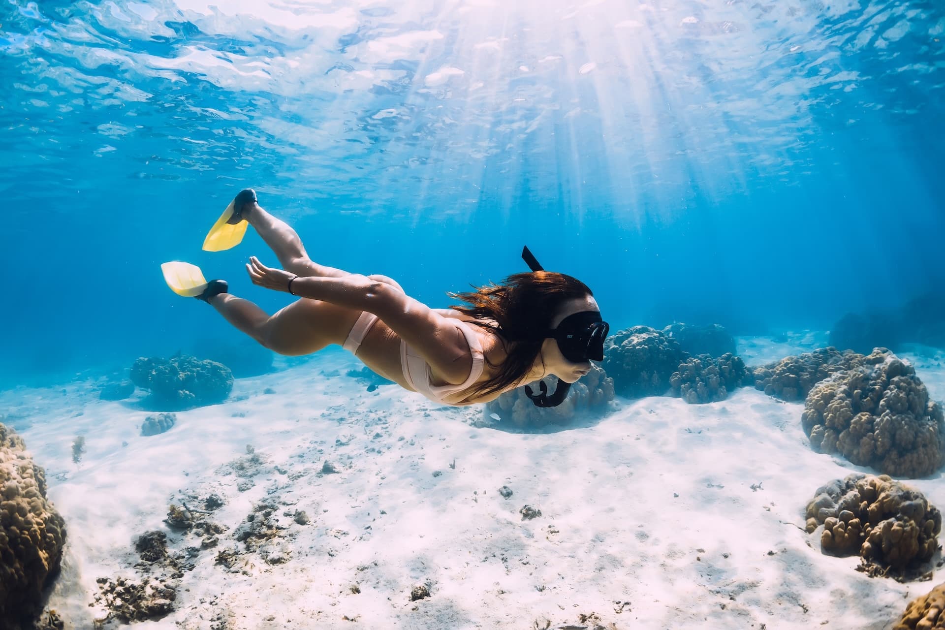 Woman snorkeling with yellow fins over white sand and coral in clear blue water, Croatia.