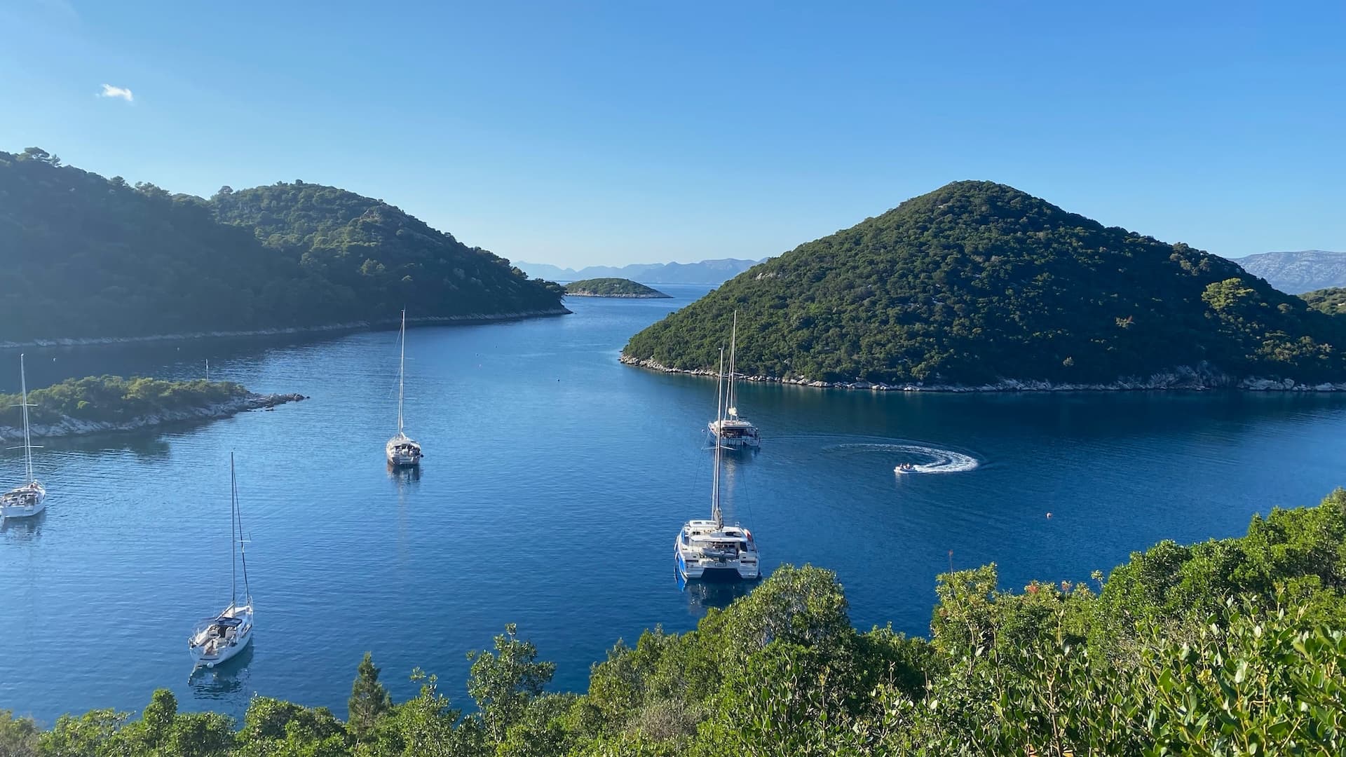 Sailboats and a catamaran anchored in blue water between lush green Croatian islands.