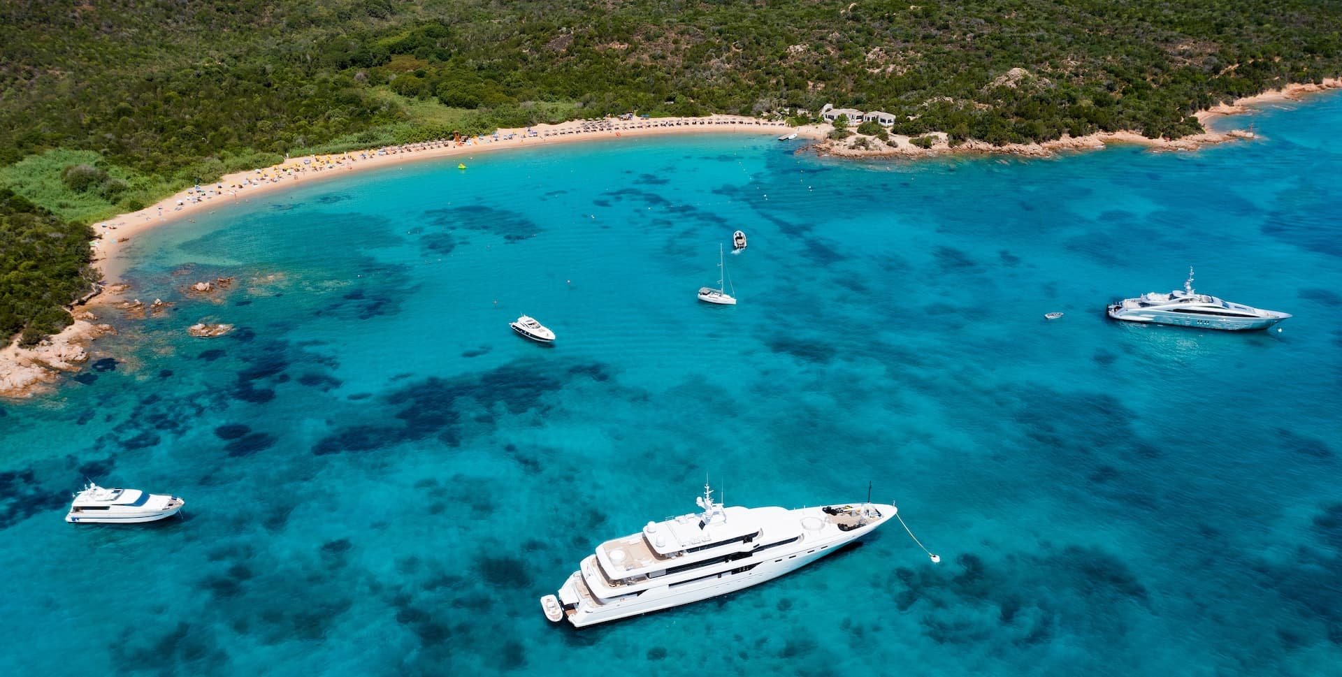 Yachts anchored in turquoise cove near sandy beach with lush green coastline
