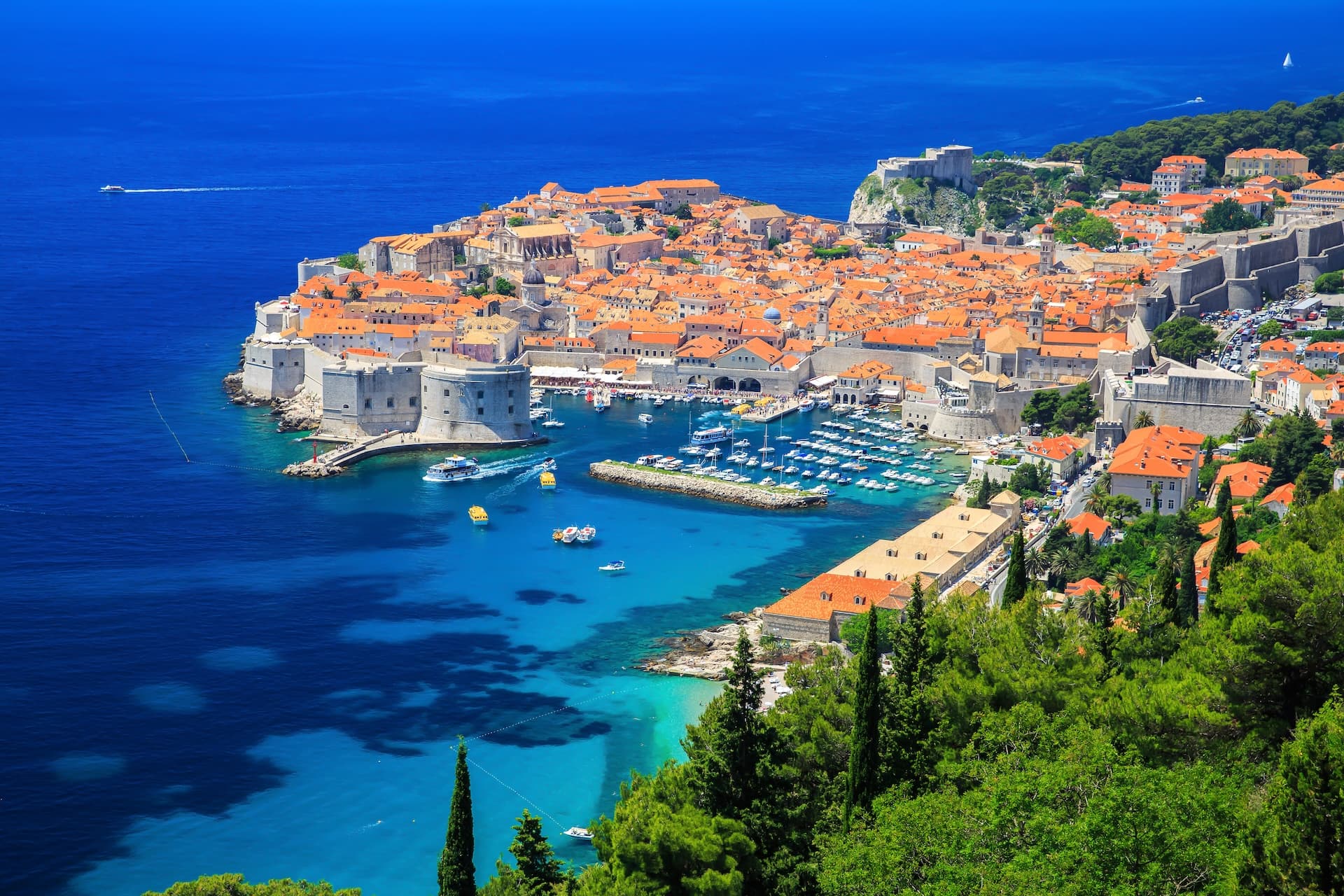 Dubrovnik Bay marina with historic walled city, orange roofs, and bright blue Adriatic Sea.