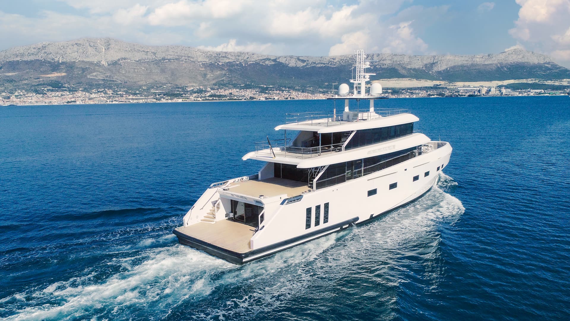 White motor yacht cruising on blue sea with coastal mountains in background