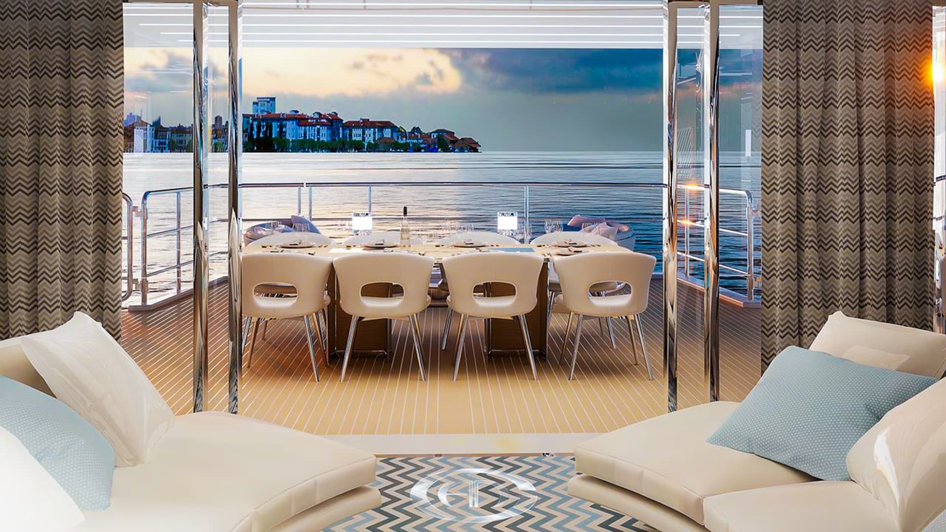 Luxury yacht interior lounge looking out to dining area and coastal town at sunset