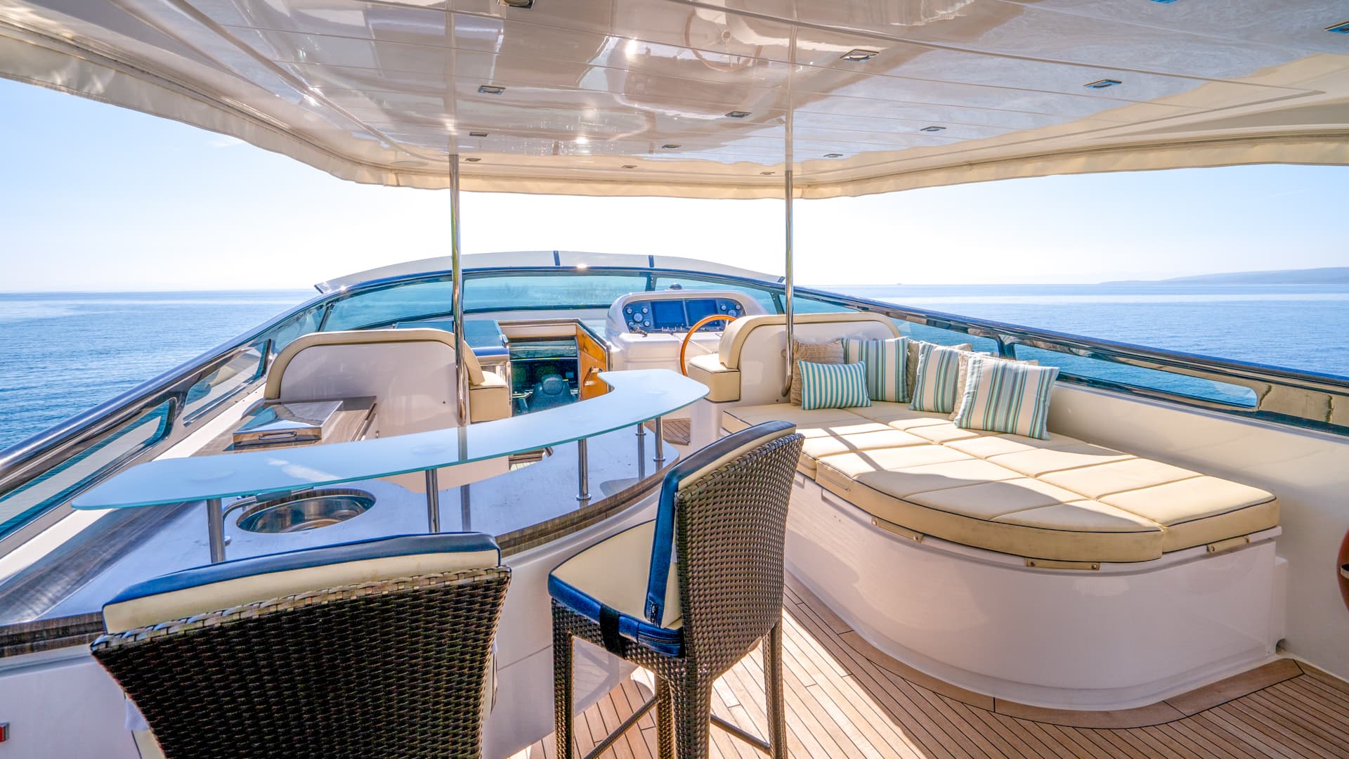 Flybridge seating area of a yacht with teak deck, sun lounge, and blue sea view.
