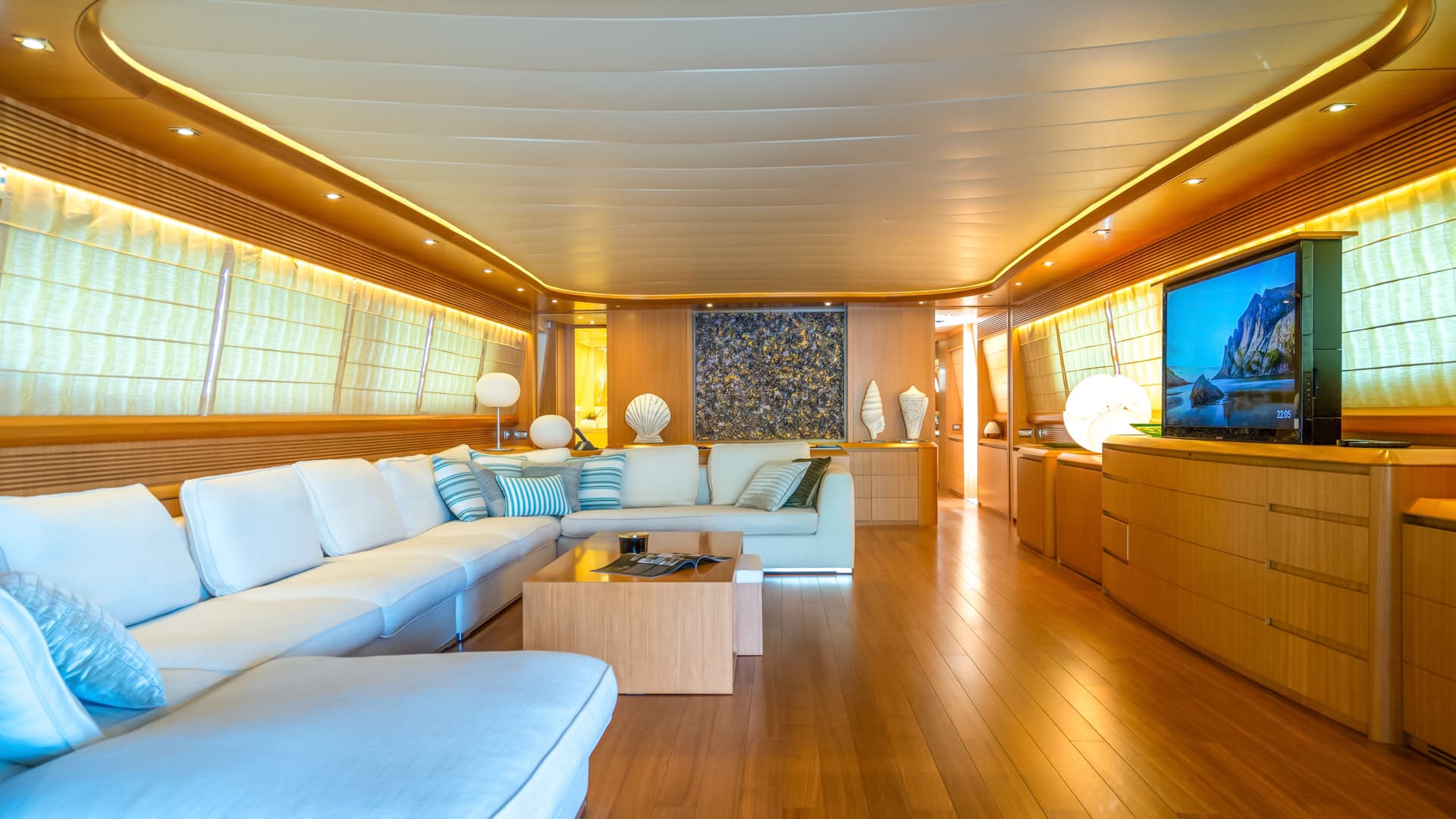 Luxurious yacht salon with white sectional sofa, wood paneling, and illuminated ceiling