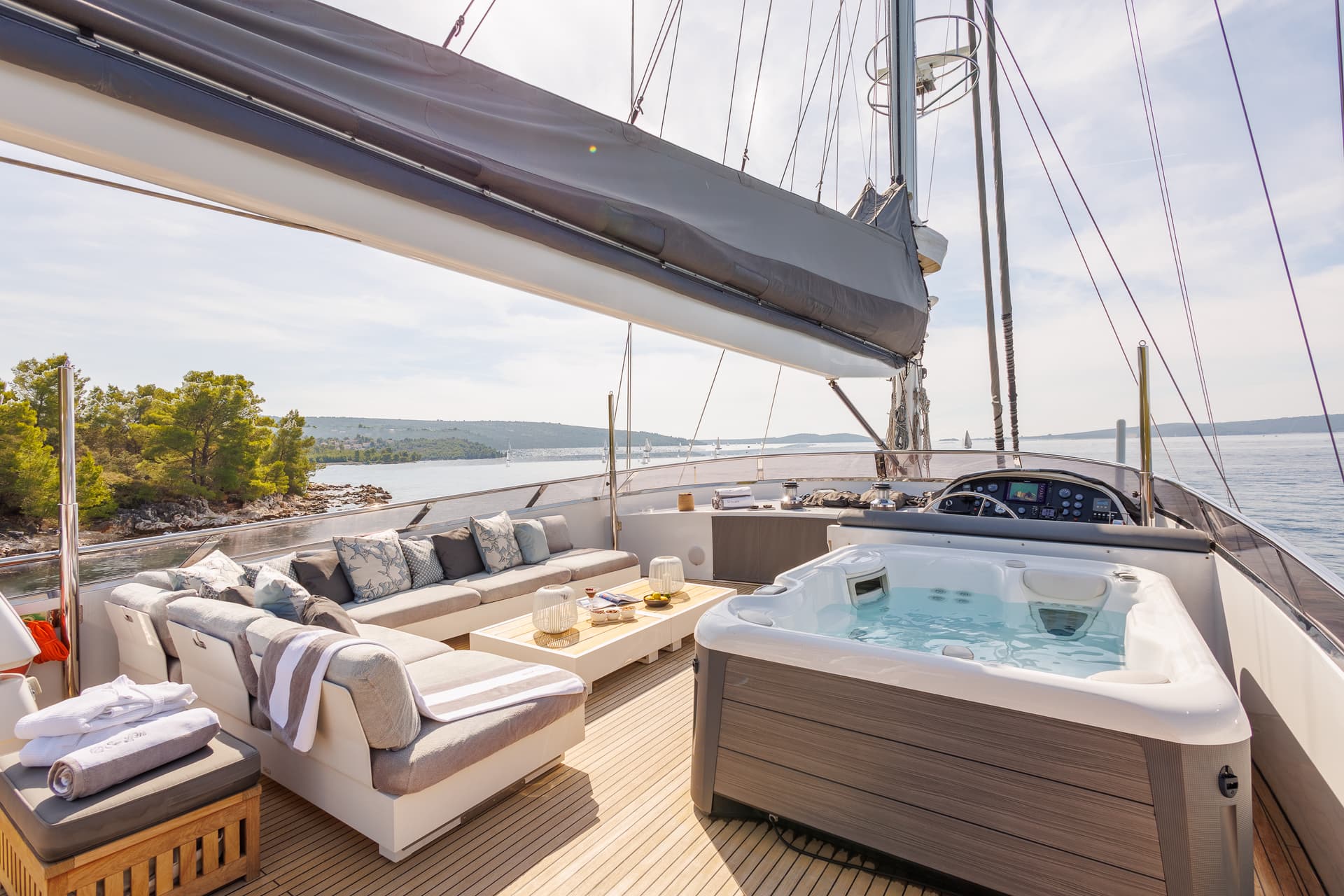 Jacuzzi and lounge seating on a sailboat deck near a wooded coastline.