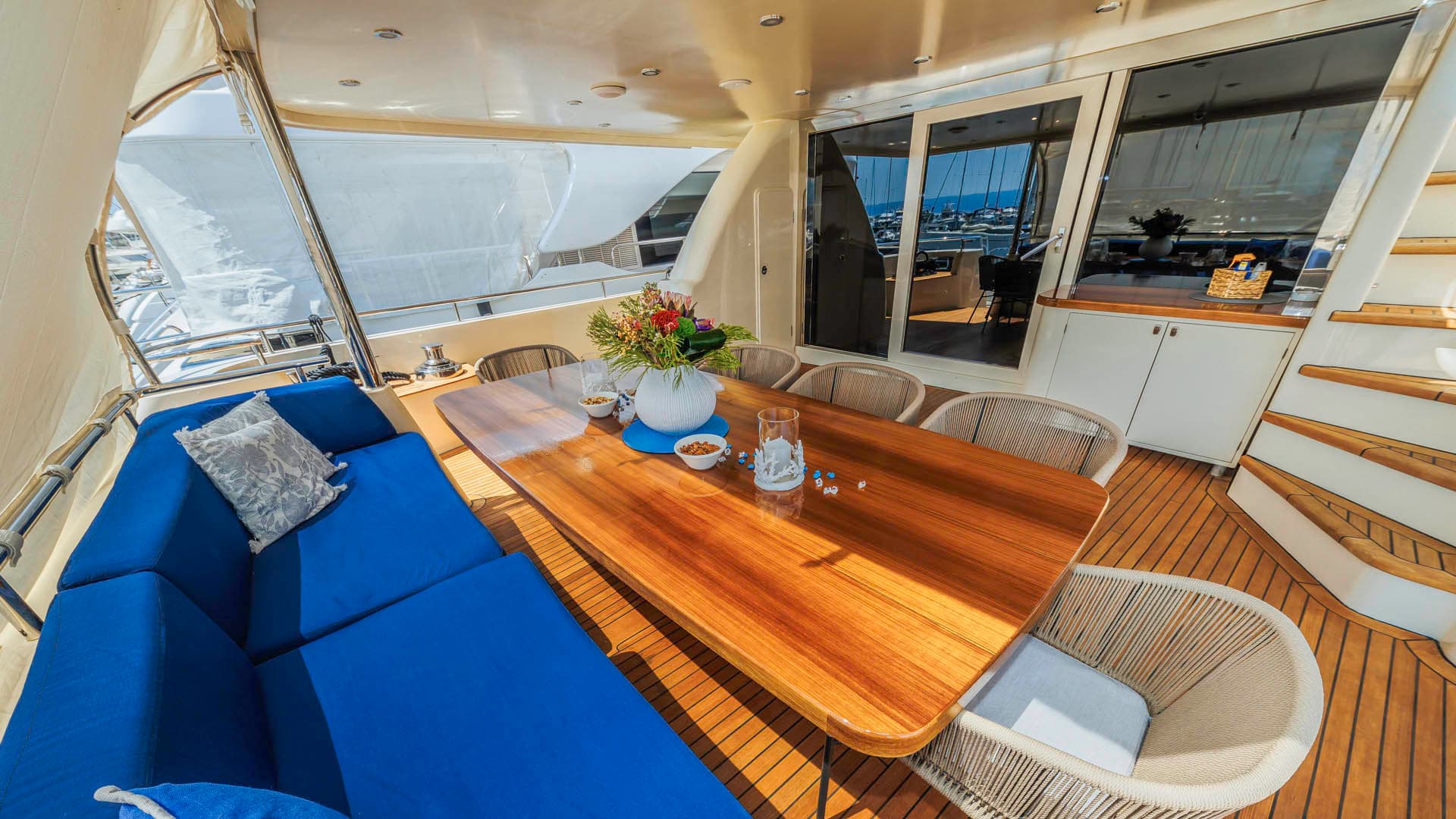 Alfresco dining area on a yacht with teak decking, blue cushions, and a wooden table.