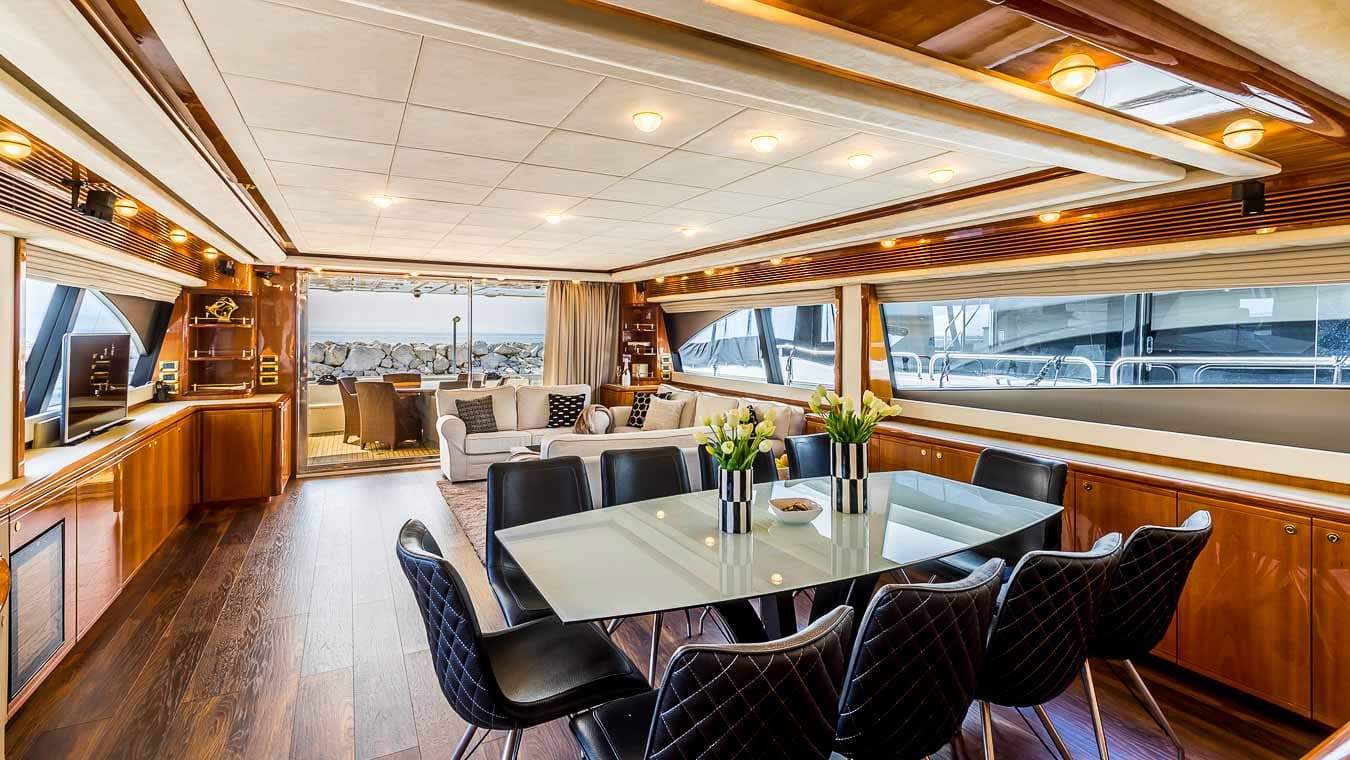 Yacht interior with dining area, lounge, and view of rocky coastline outside