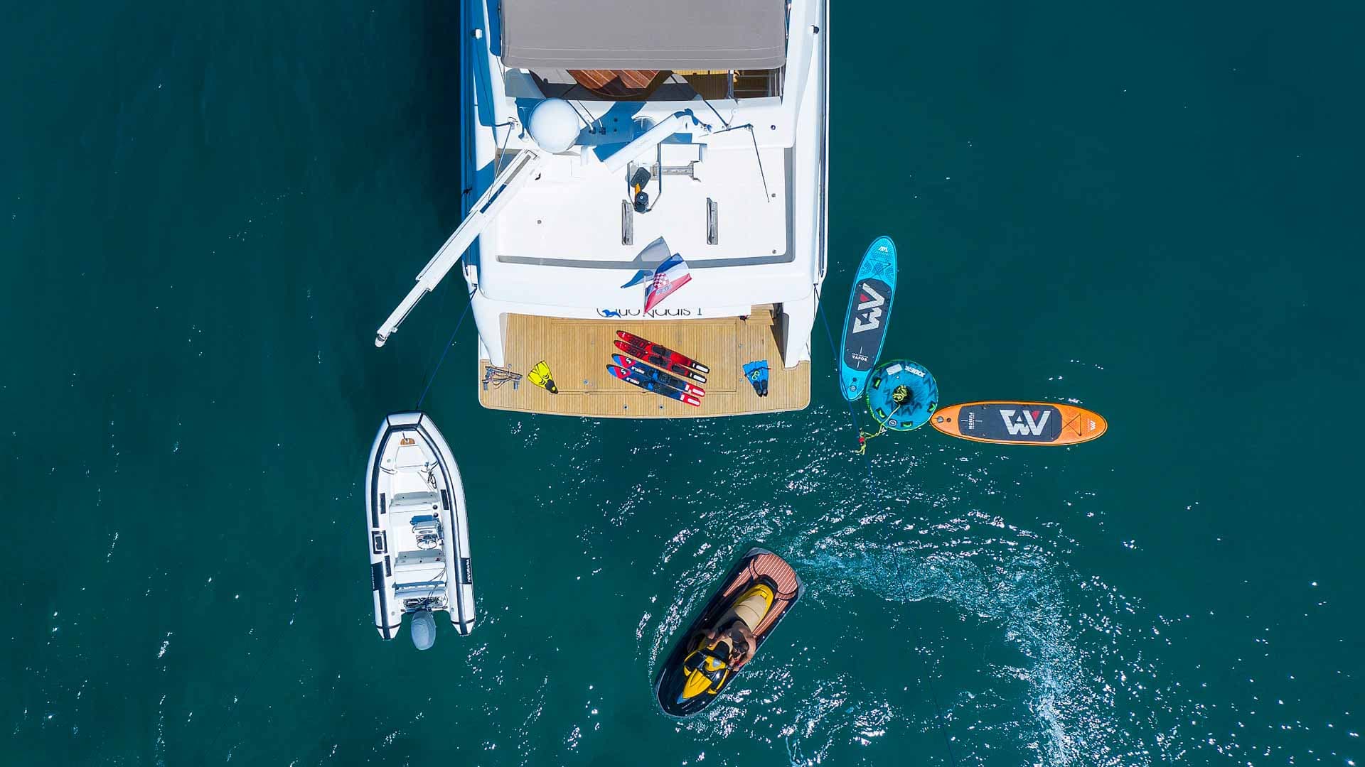 Yacht stern with water toys, dinghy, jet ski, and paddleboards on turquoise water