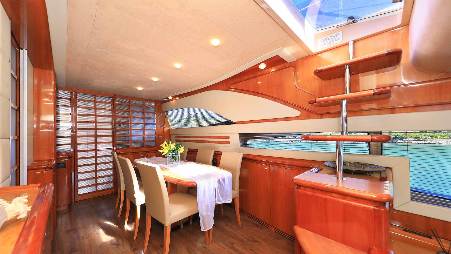 Yacht dining area with wood paneling, set table, and view of turquoise water.