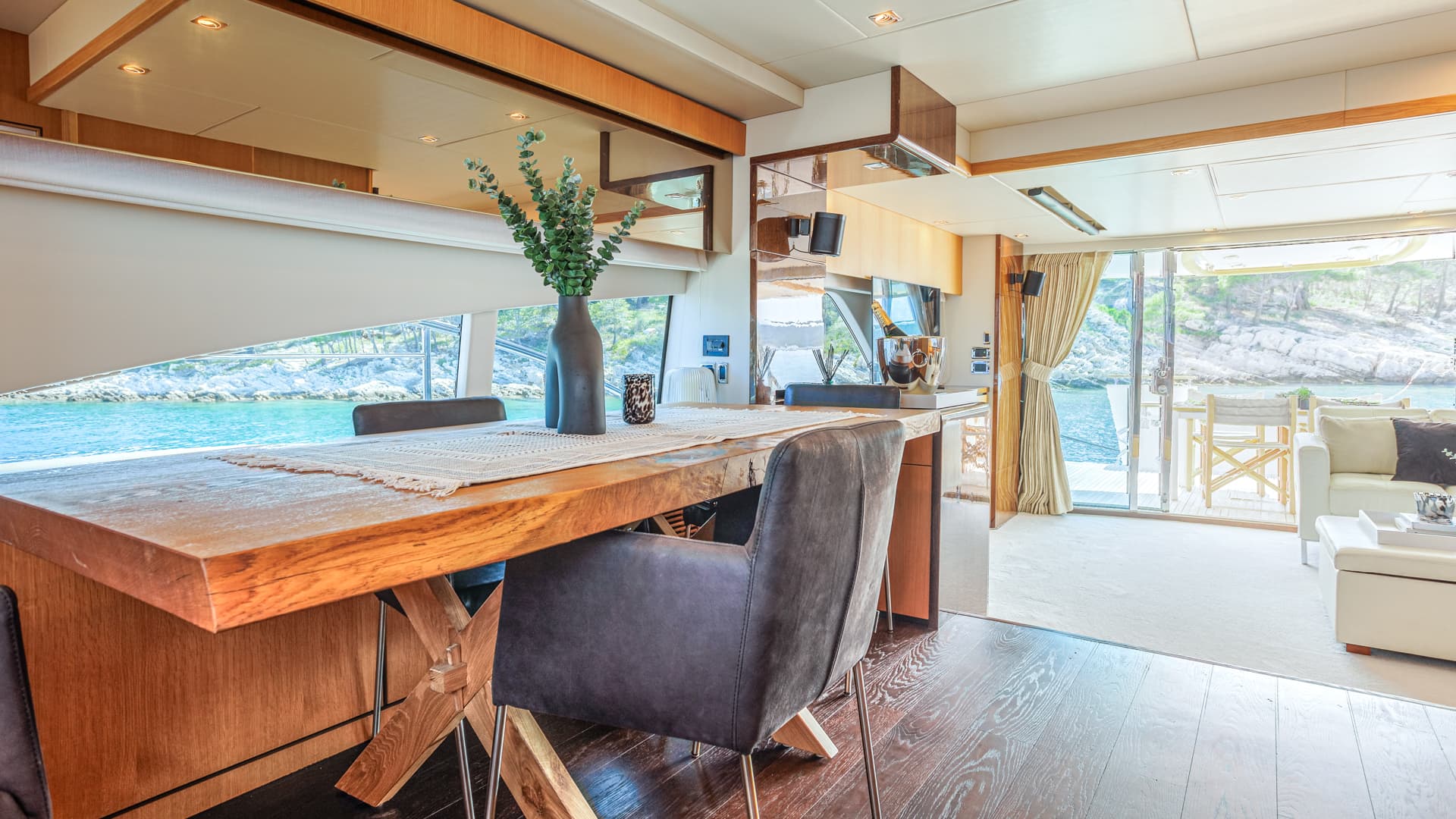 Yacht dining area with wooden table overlooking rocky coastline and turquoise water