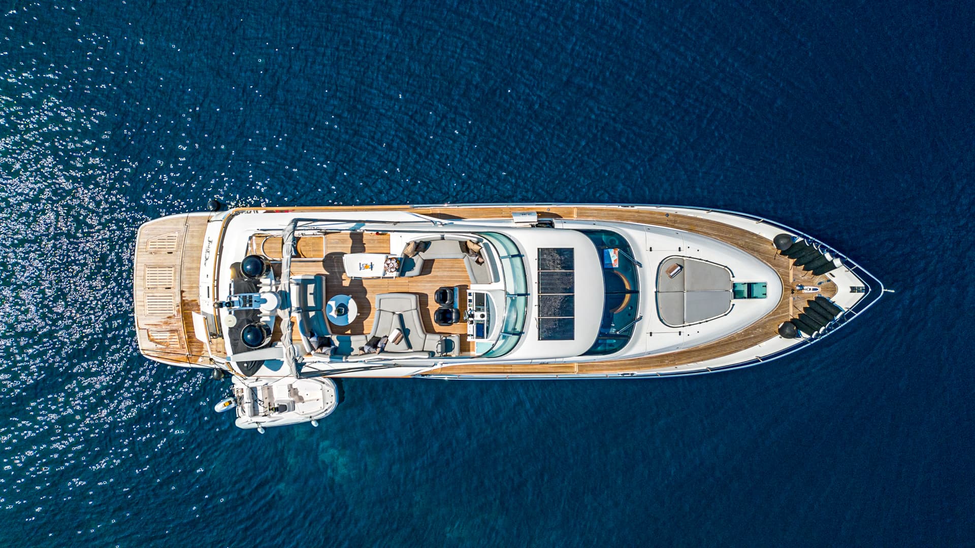 Aerial view of luxury motor yacht with wooden deck anchored in deep blue, sparkling water.