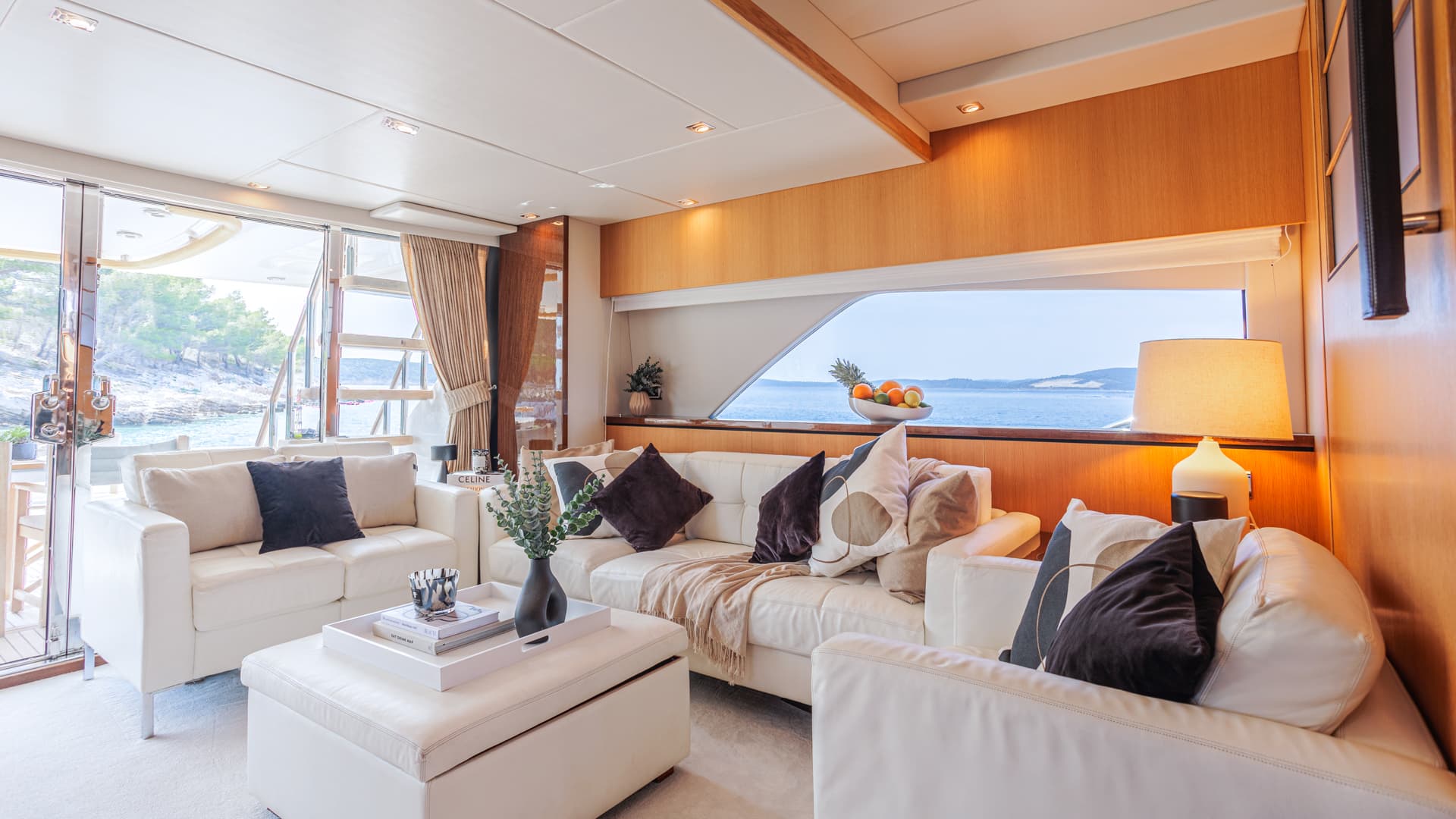 Yacht salon with white leather seating overlooking a wooded coastline and blue sea