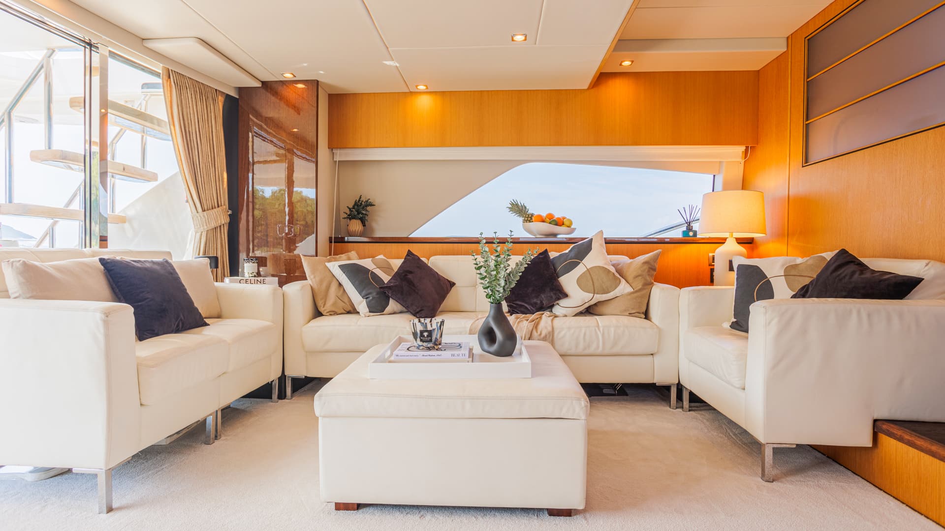 Luxury yacht salon interior with white leather sofas, wood paneling, and view of exterior stairs.