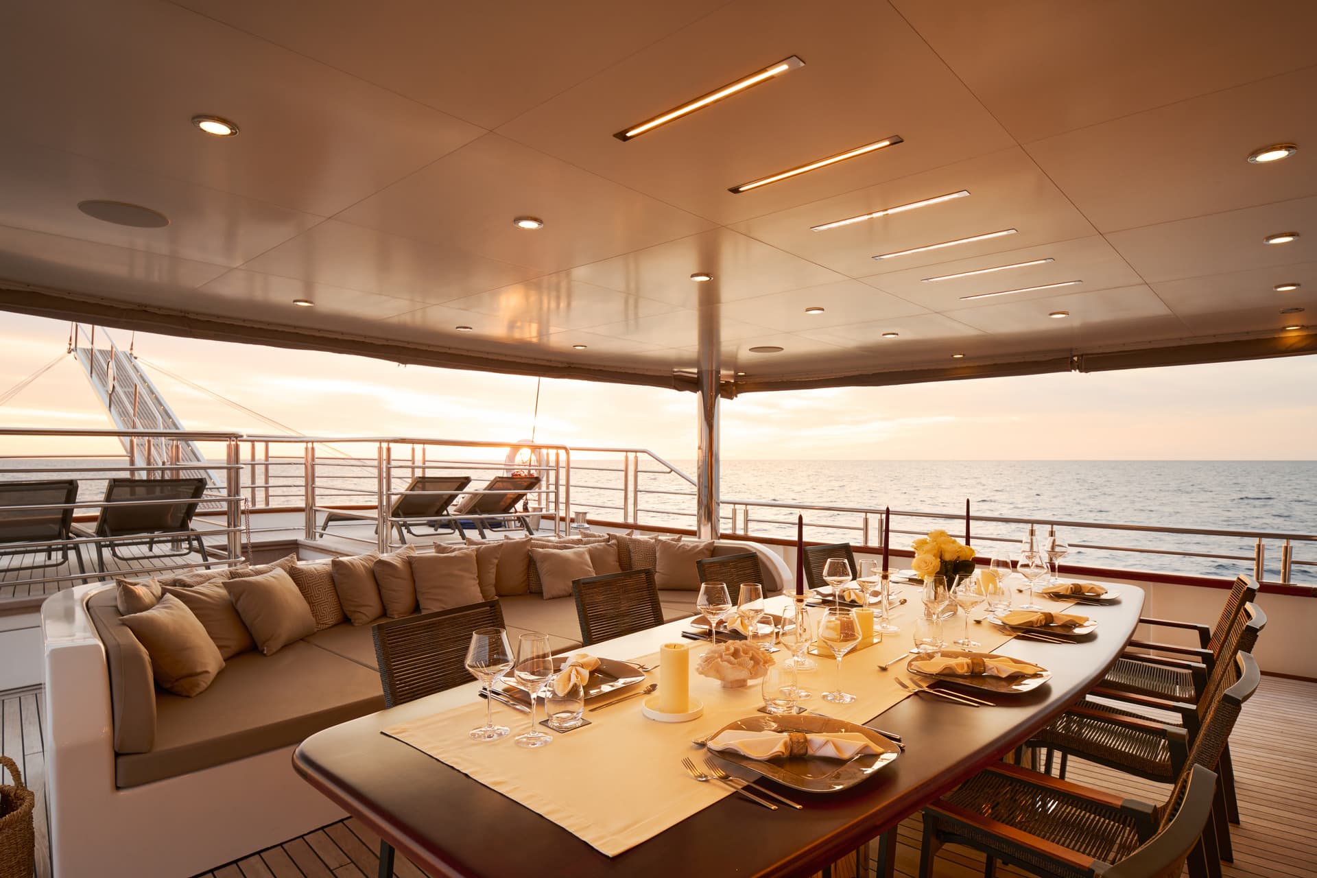 Outdoor dining area set on a yacht deck overlooking the sea at sunset