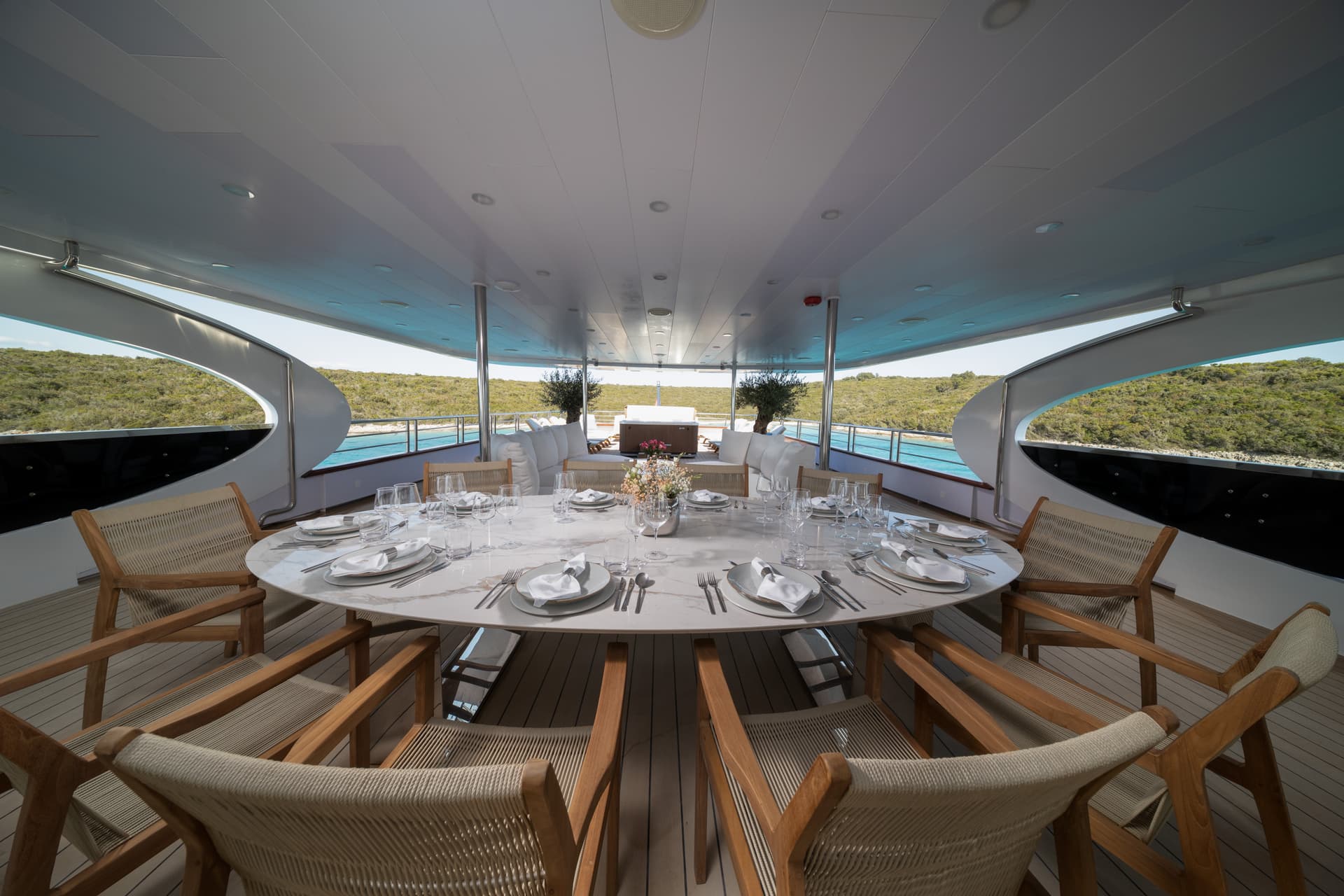 Outdoor dining area on a yacht with a set marble table overlooking a lush, green coastline.