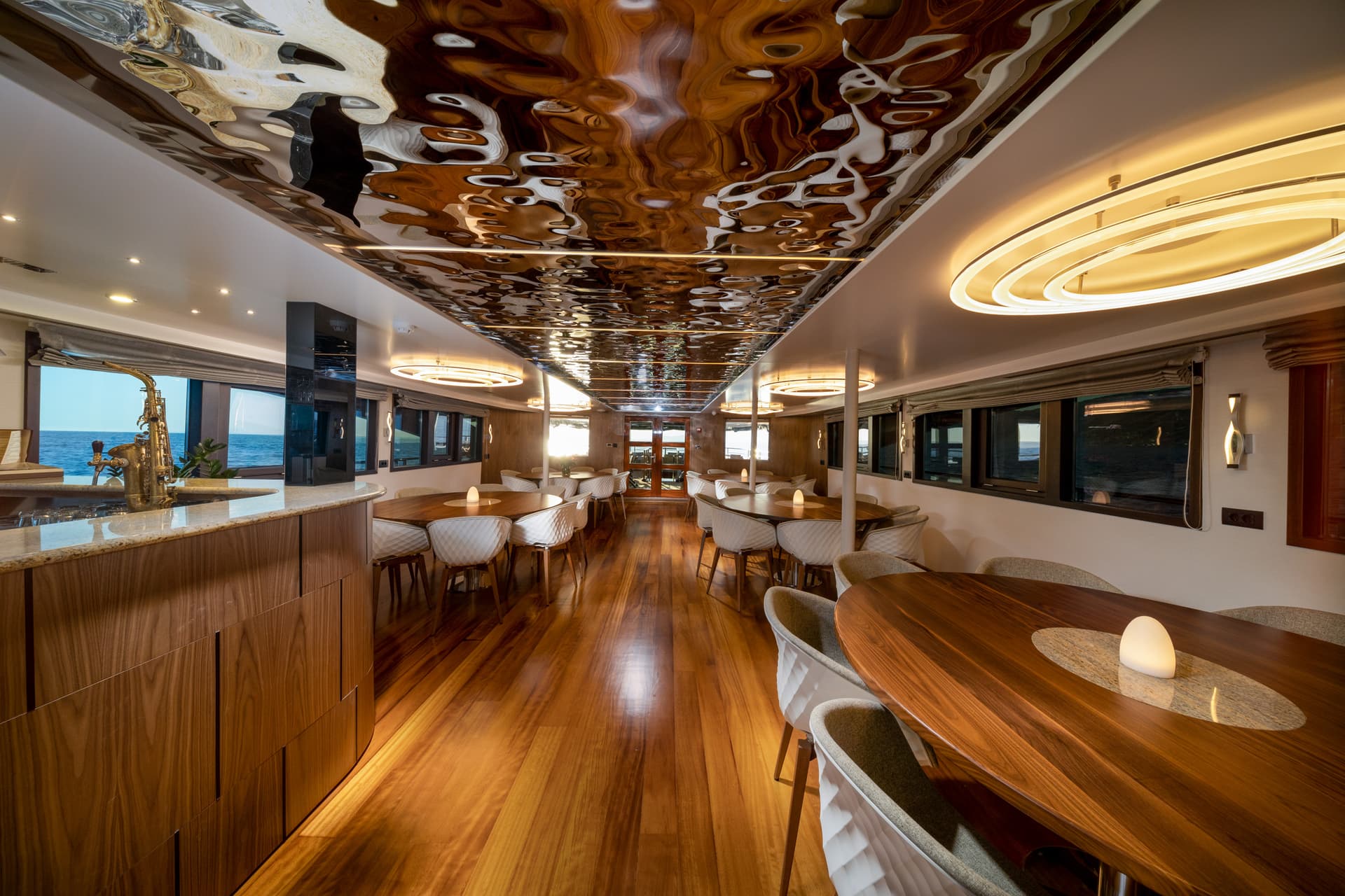 Dining area on a yacht with wood floors, modern chairs, and sea view through windows.