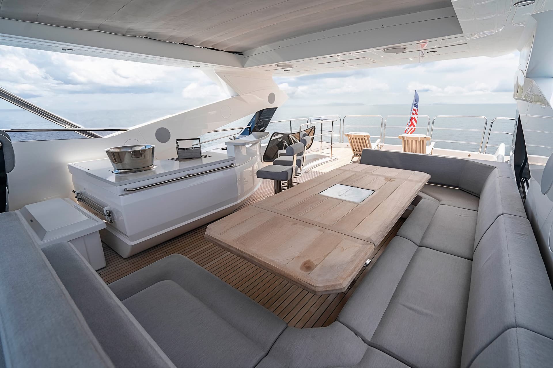 Outdoor seating area on a yacht deck with gray cushions, wooden table, and ocean view.