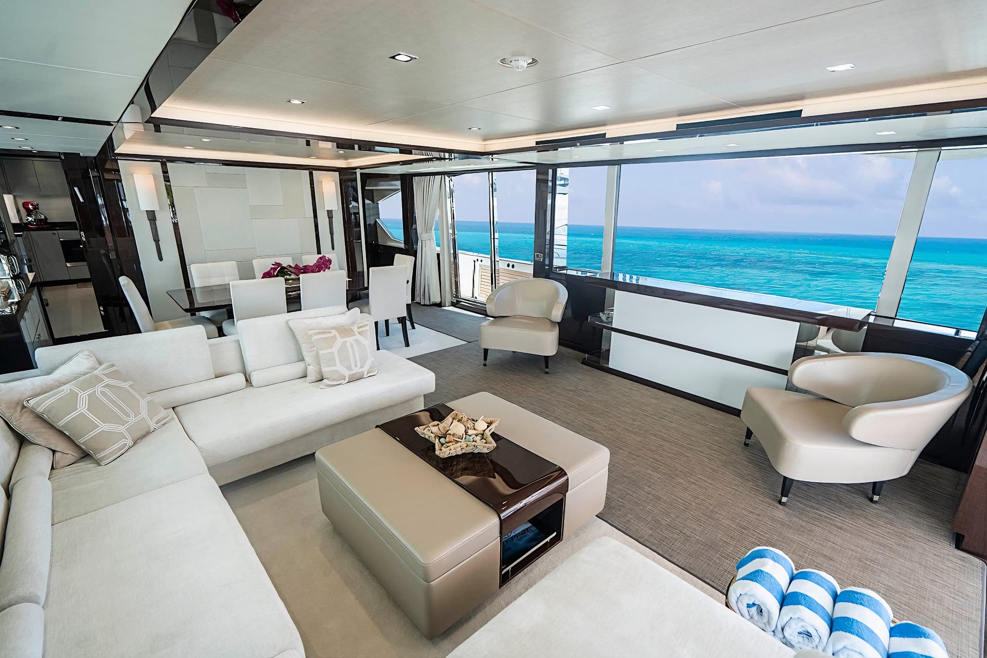 Luxury yacht interior lounge with white seating and view of turquoise ocean water.