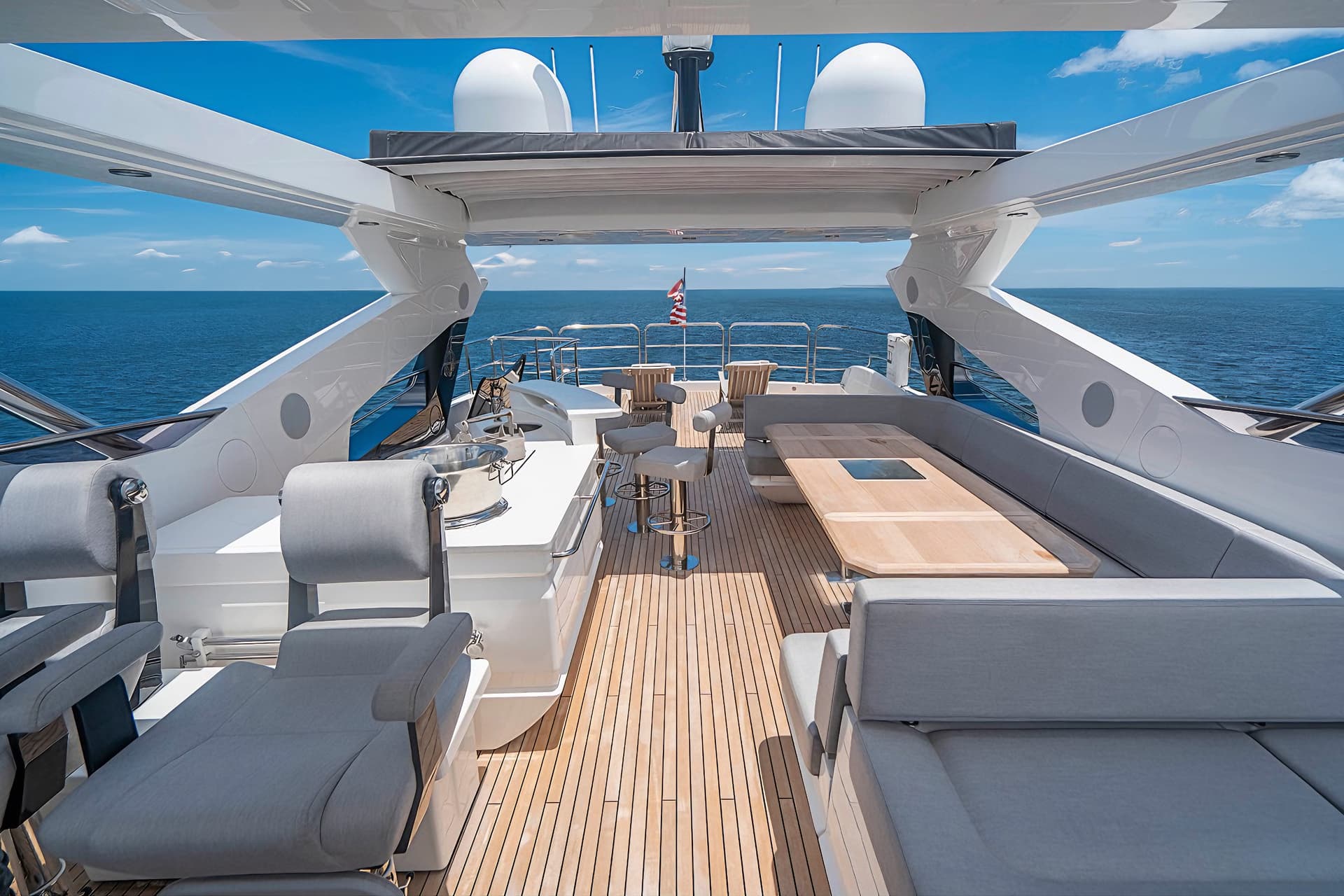 Luxury yacht aft deck with teak flooring, grey seating, and open blue sea view