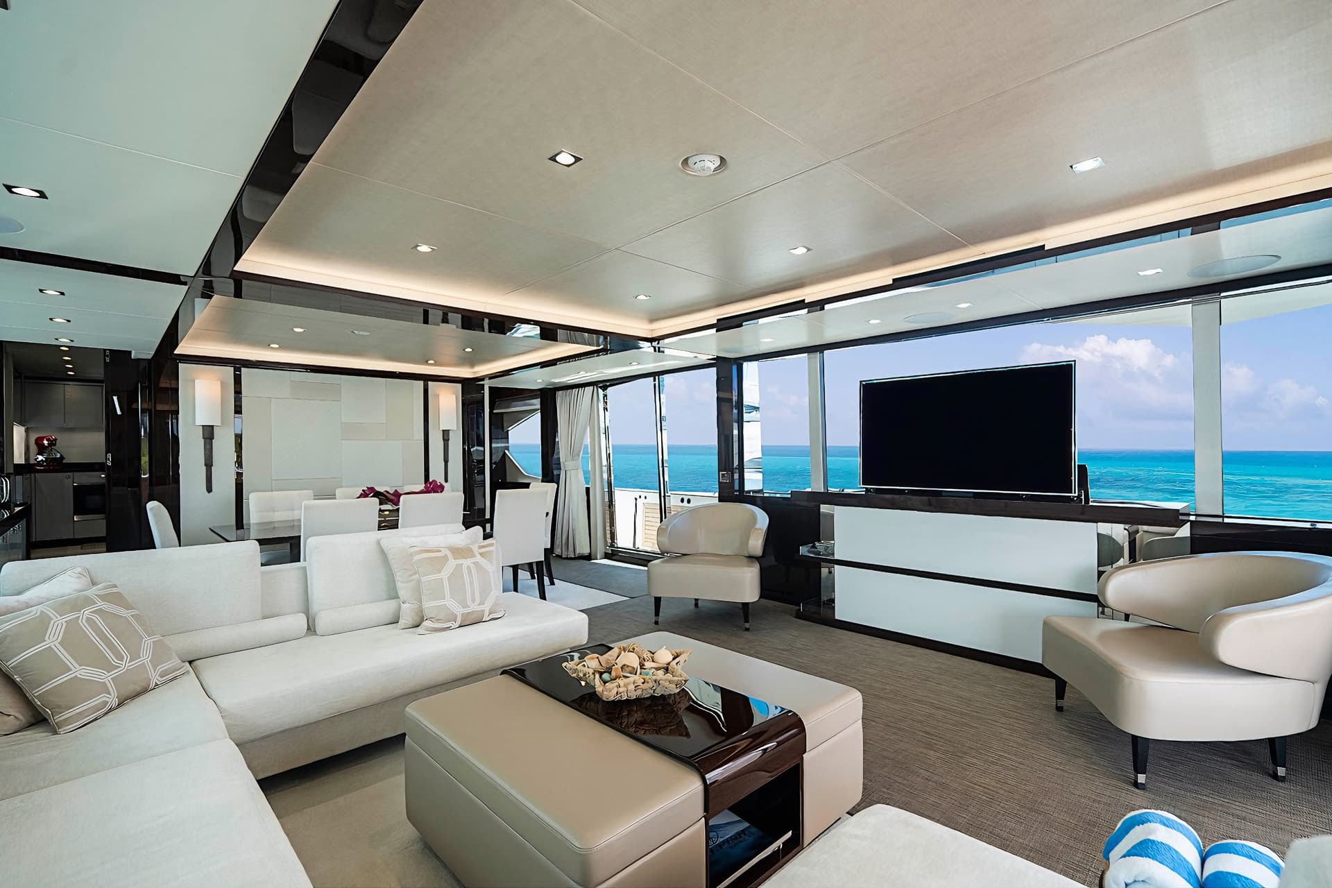 Luxury yacht interior lounge with modern white seating overlooking turquoise ocean water.