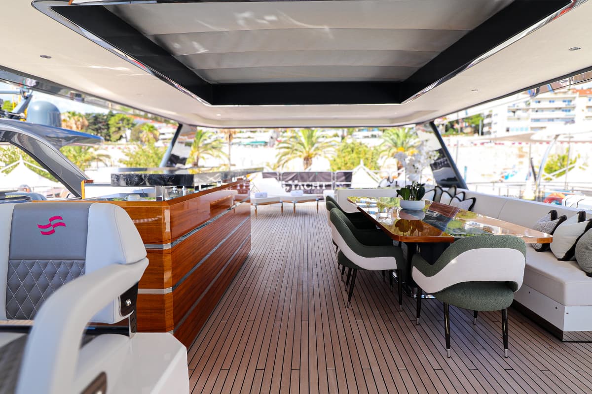 Flybridge deck with teak flooring, dining area, and palm trees visible ashore.