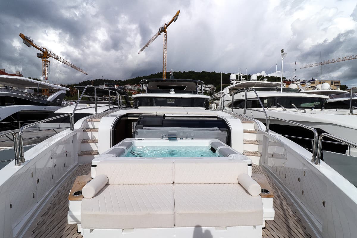 Foredeck jacuzzi and lounge seating on a yacht docked near other boats with construction cranes visible.