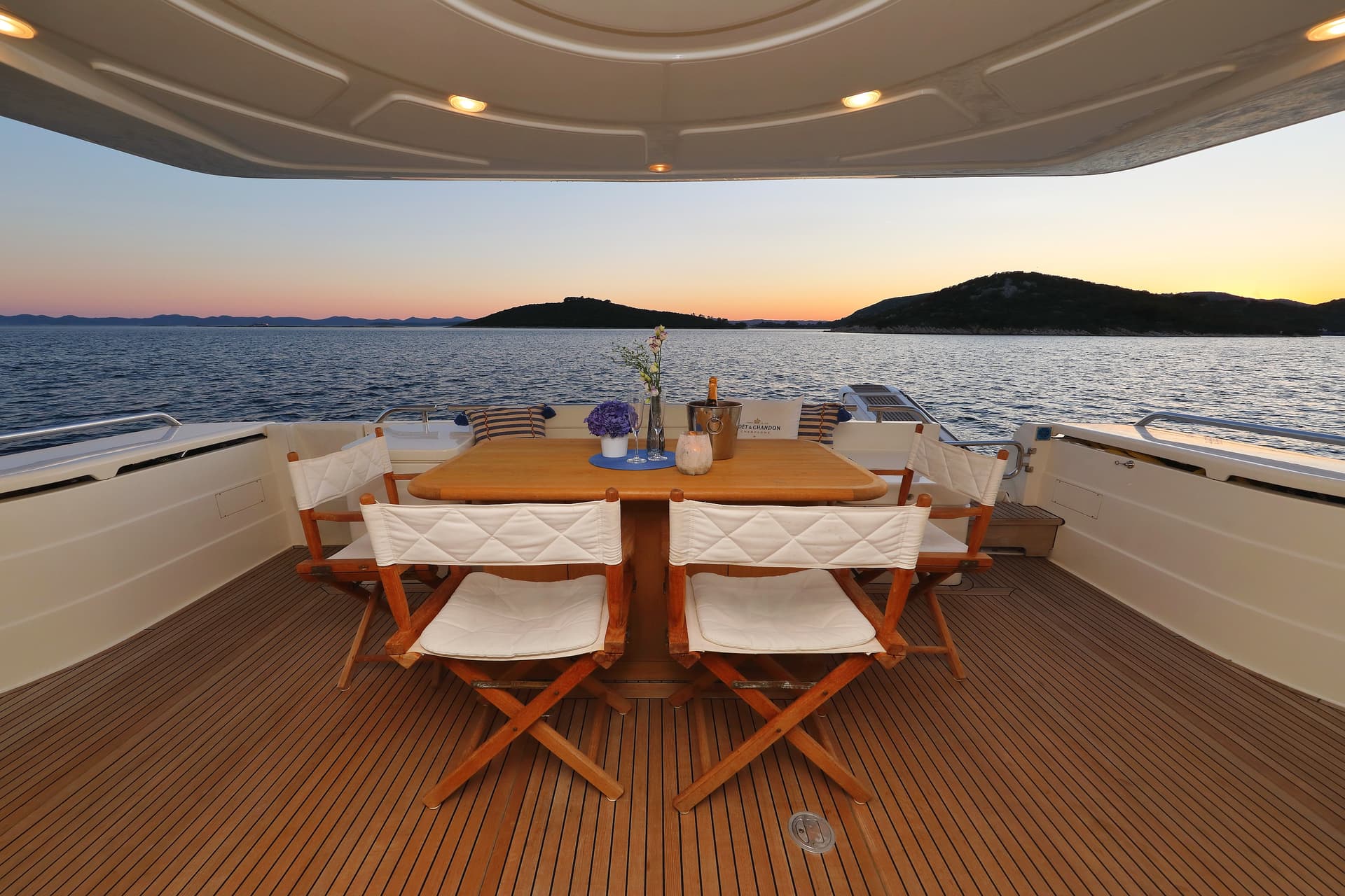 Yacht aft deck dining setup with champagne overlooking islands at sunset