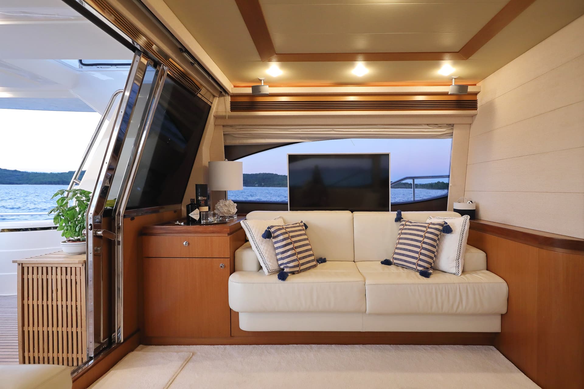 Yacht interior saloon with white leather couch looking out at water and forested shoreline.