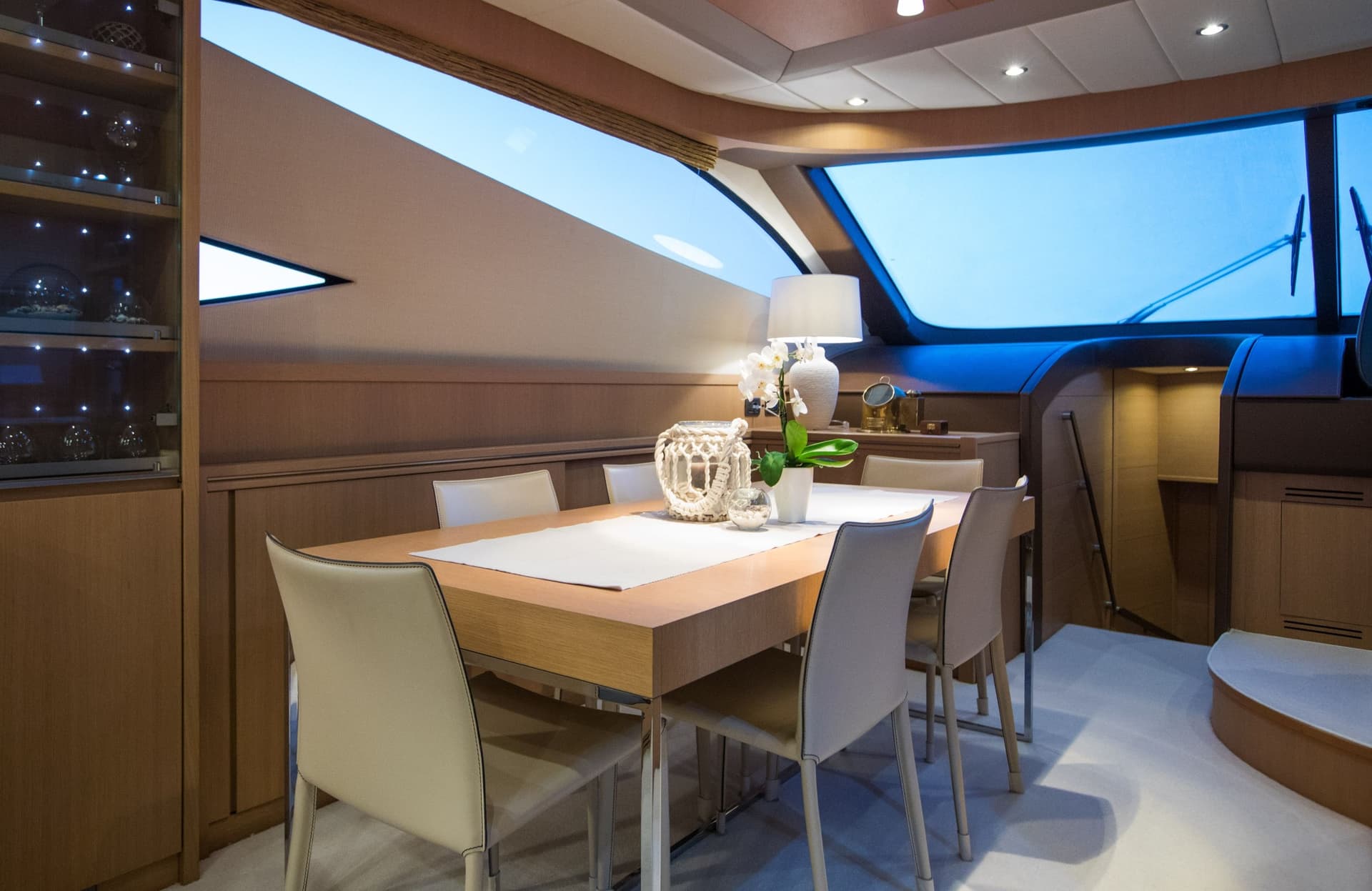 Dining area inside a yacht with wood paneling and bright blue windows.