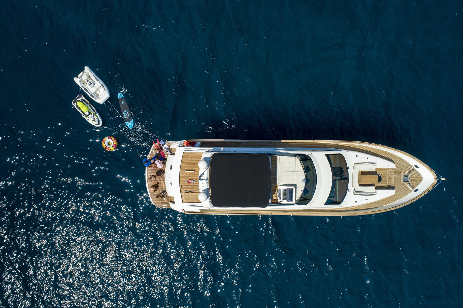Aerial view of yacht with water toys and people on deck floating on deep blue sea.