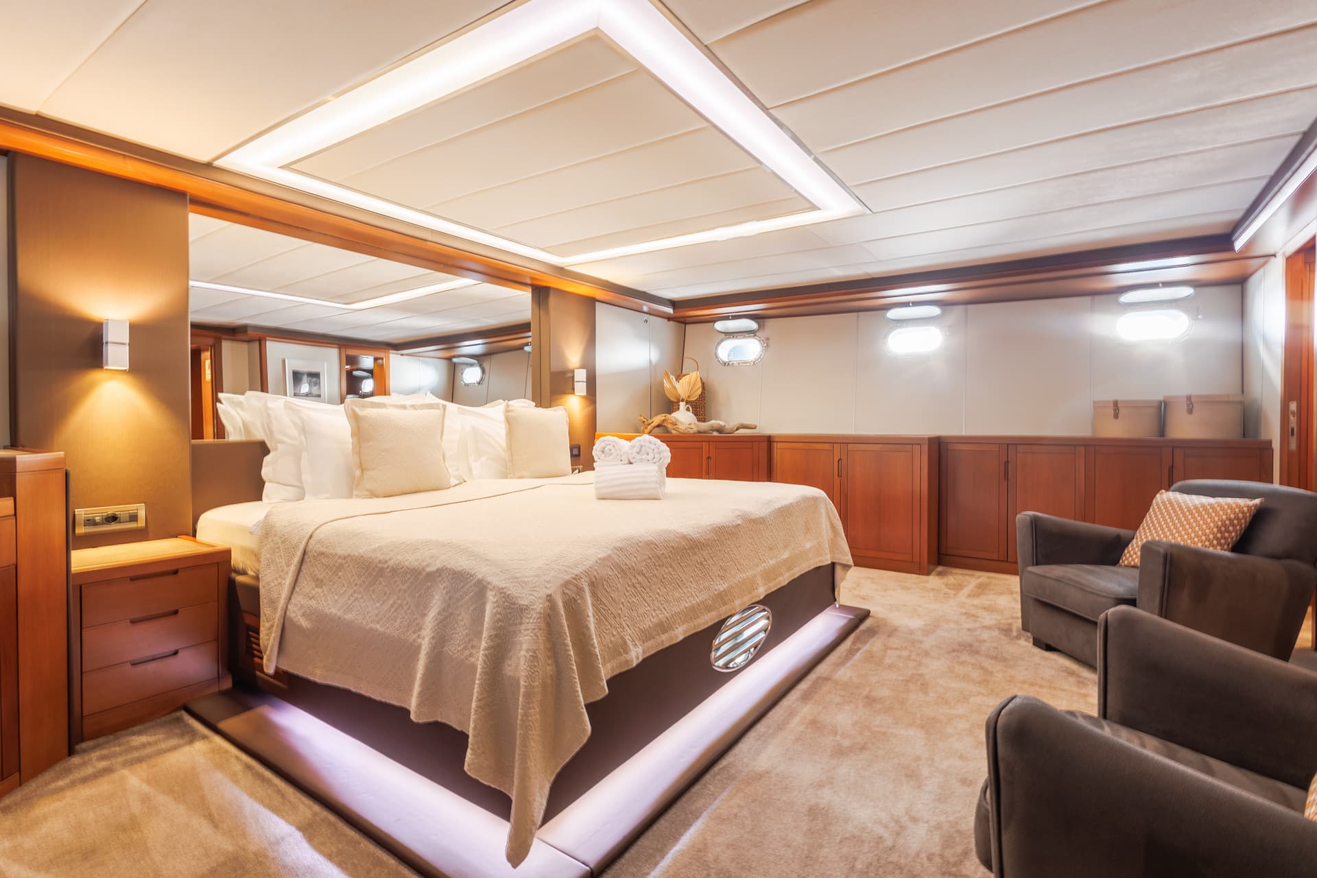 Master cabin interior with large bed, wood cabinetry, and oval porthole windows on a yacht.