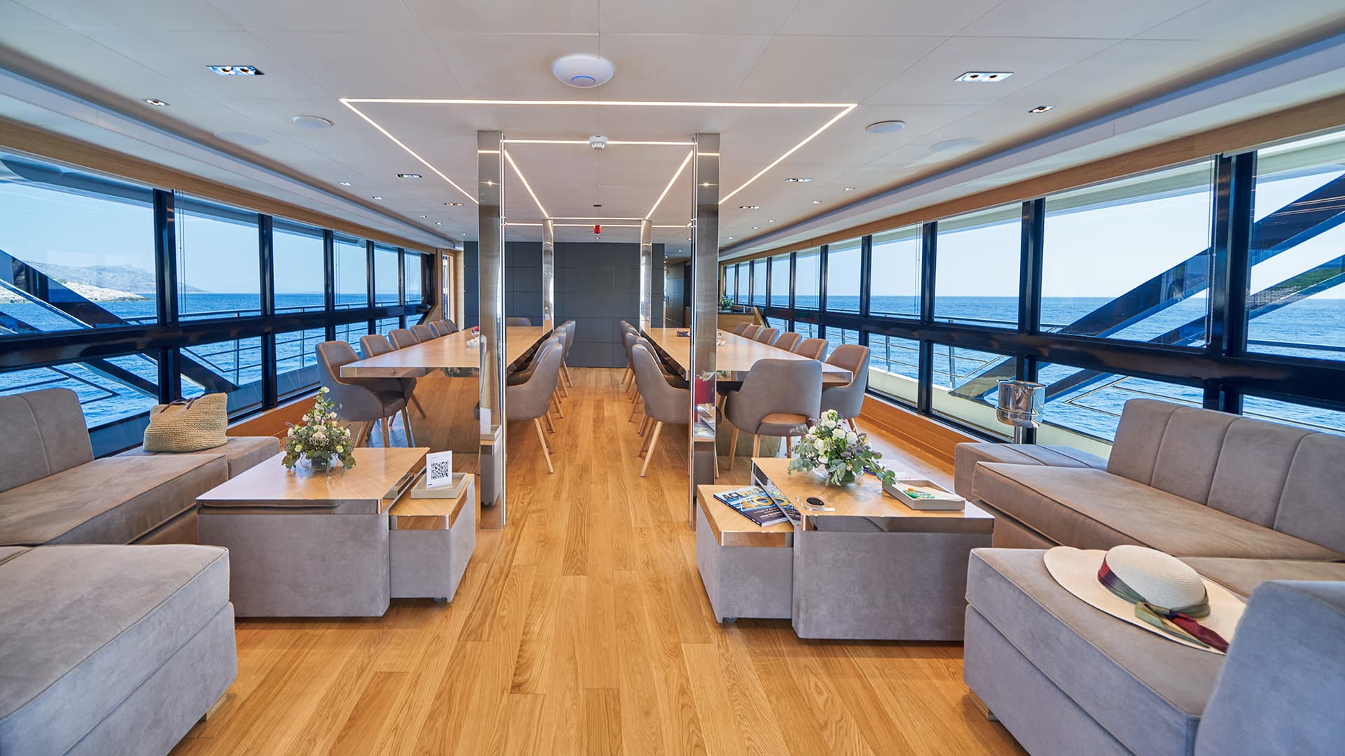 Luxury yacht interior lounge with dining tables and ocean view, likely in the Mediterranean.