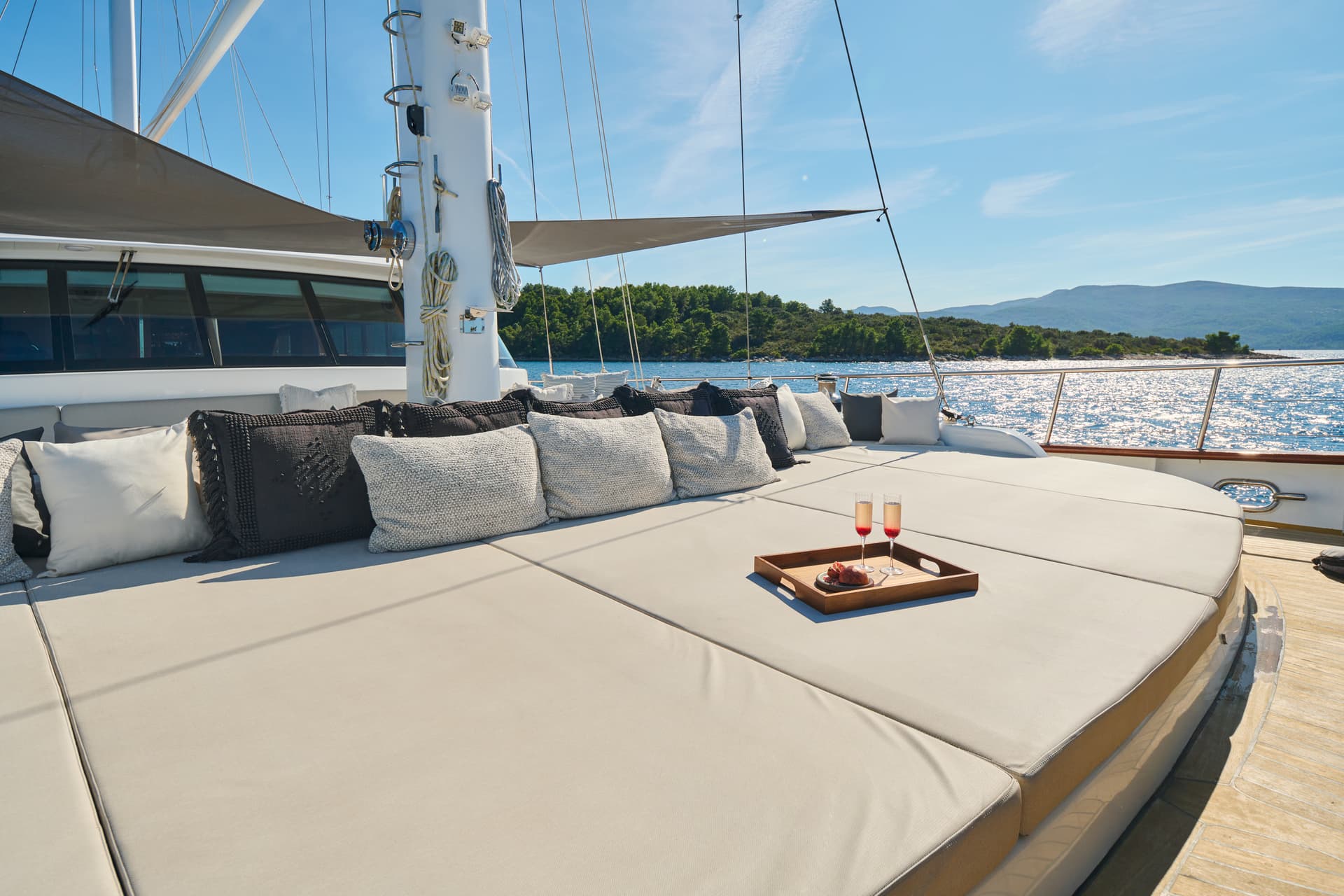 Yacht sun deck with champagne and fruit tray overlooking forested coastline on sunny day