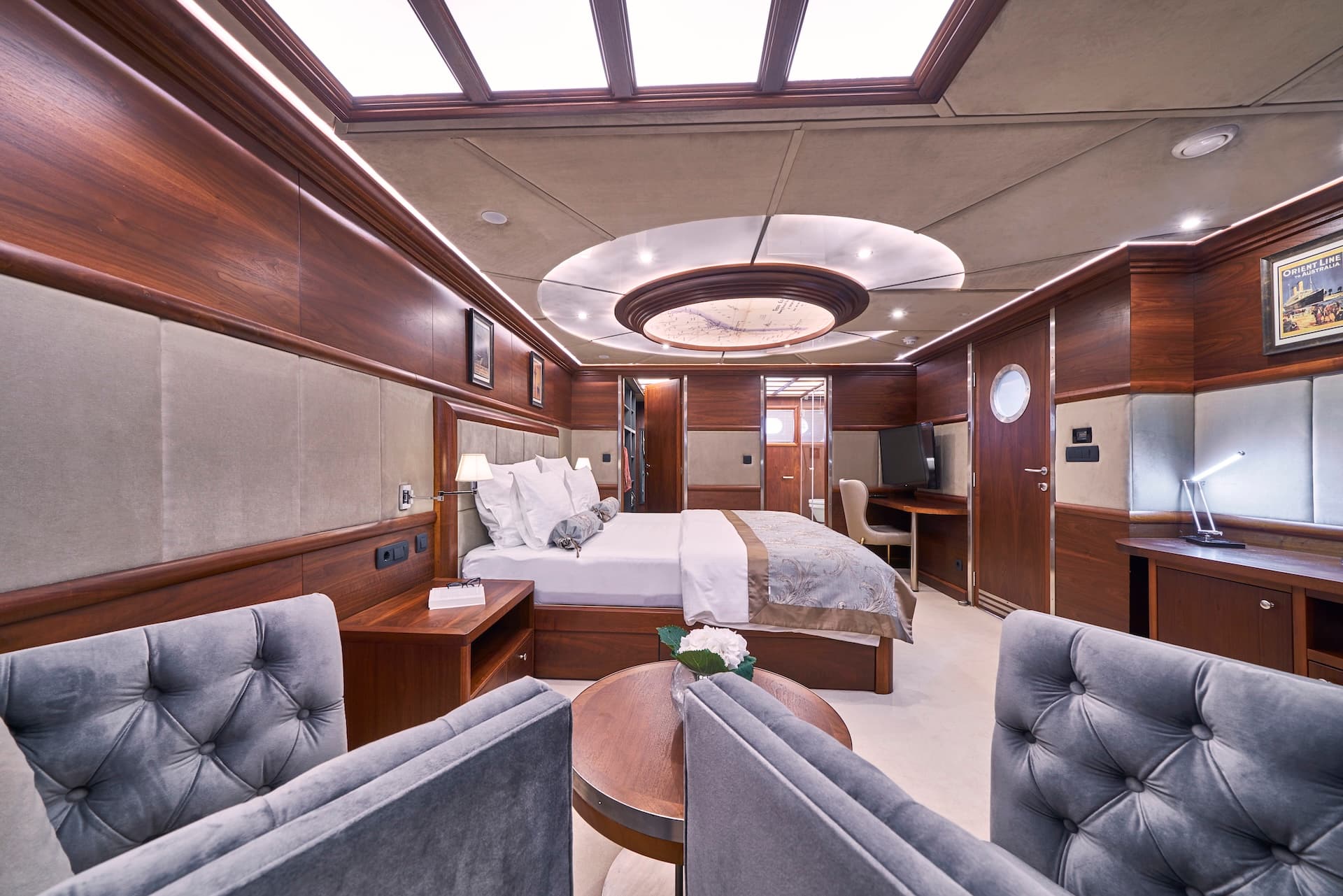 Master cabin interior with rich wood paneling, plush seating, and porthole door on a vessel.