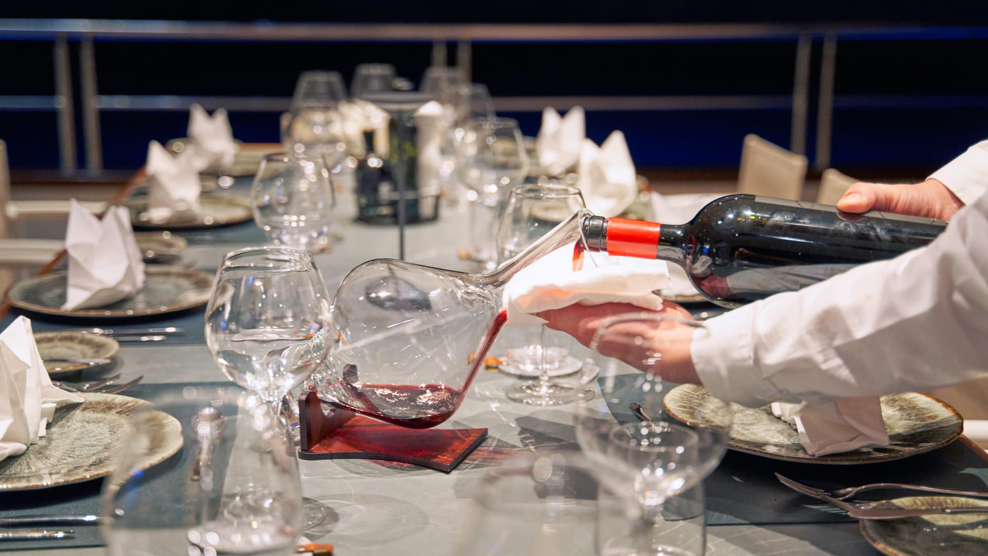 Waiter decanting red wine from a bottle into a glass carafe at a formal dining table setting.
