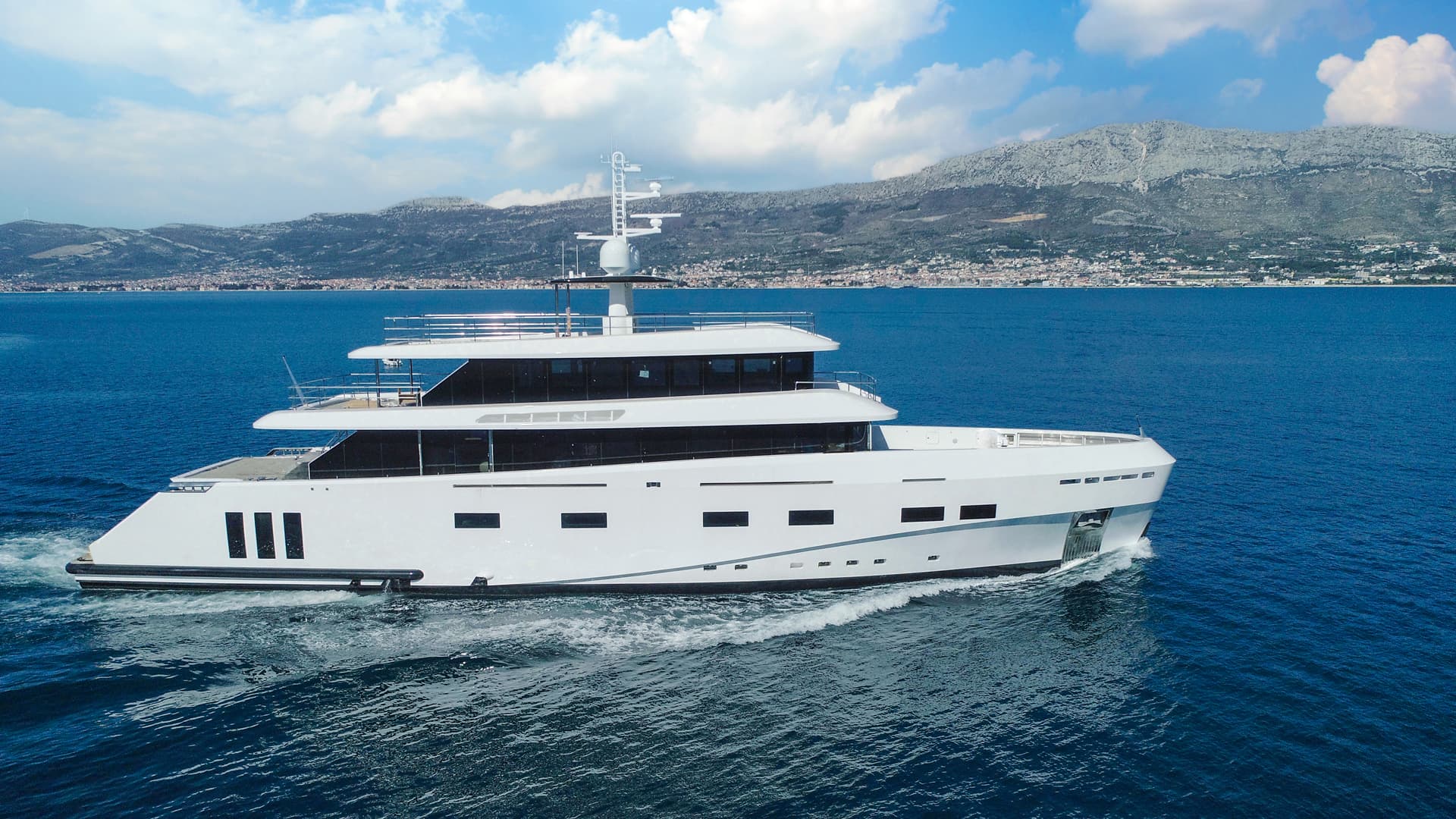 White motor yacht cruising on deep blue sea with coastal mountains in background