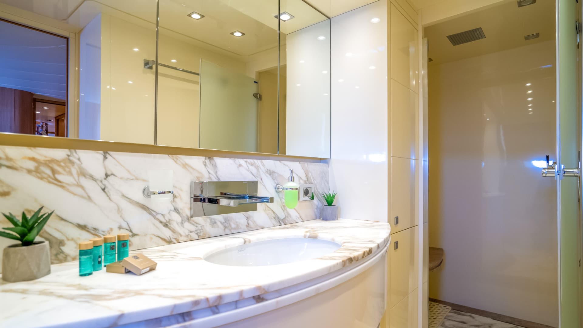 Bathroom vanity with marble countertop, sink, mirror, and open shower stall, likely on a yacht.