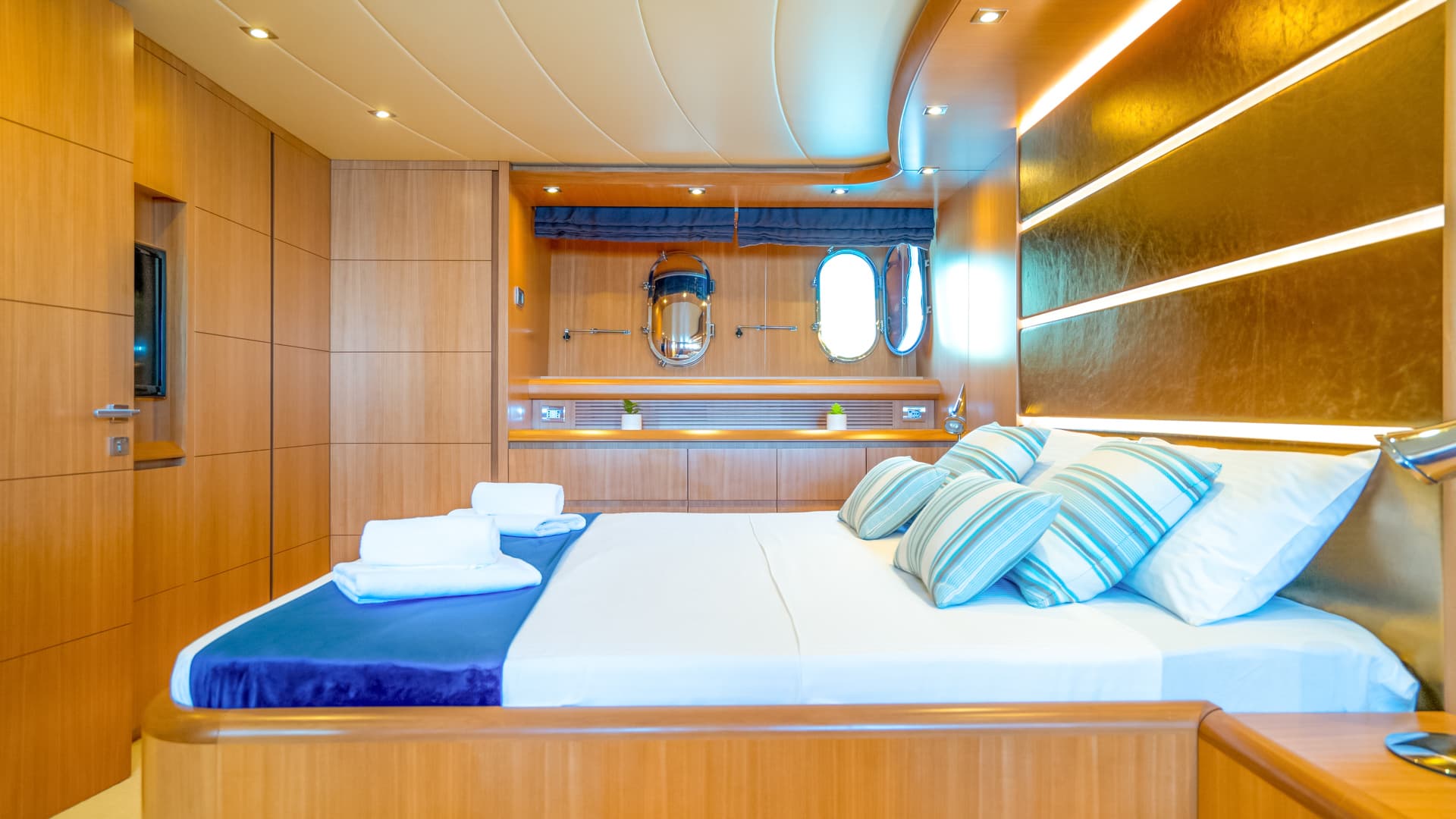 Master cabin bedroom with wood paneling, porthole windows, and illuminated headboard on a yacht.
