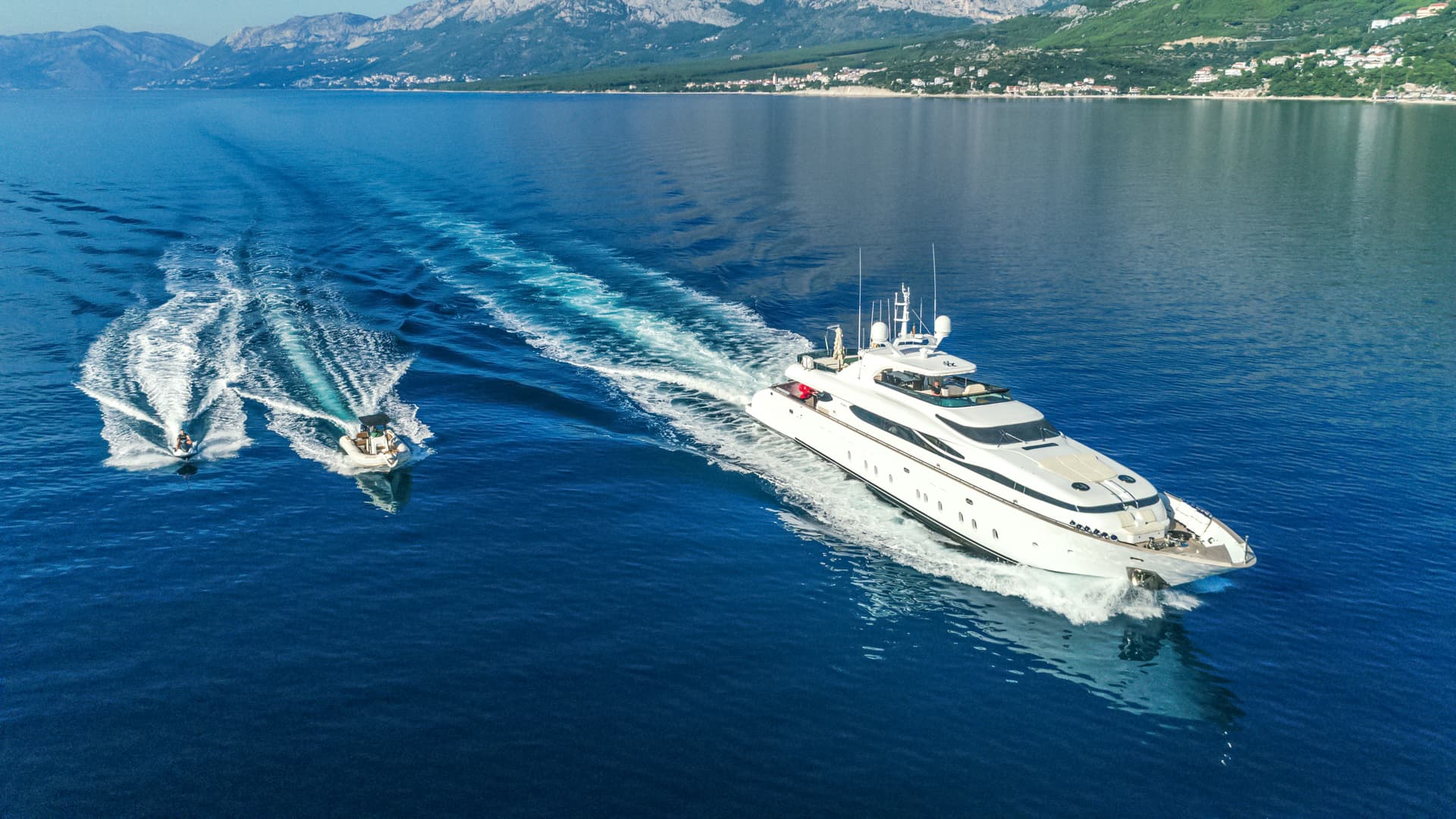 Luxury yacht and personal watercraft cruising on deep blue sea near coastline with mountains