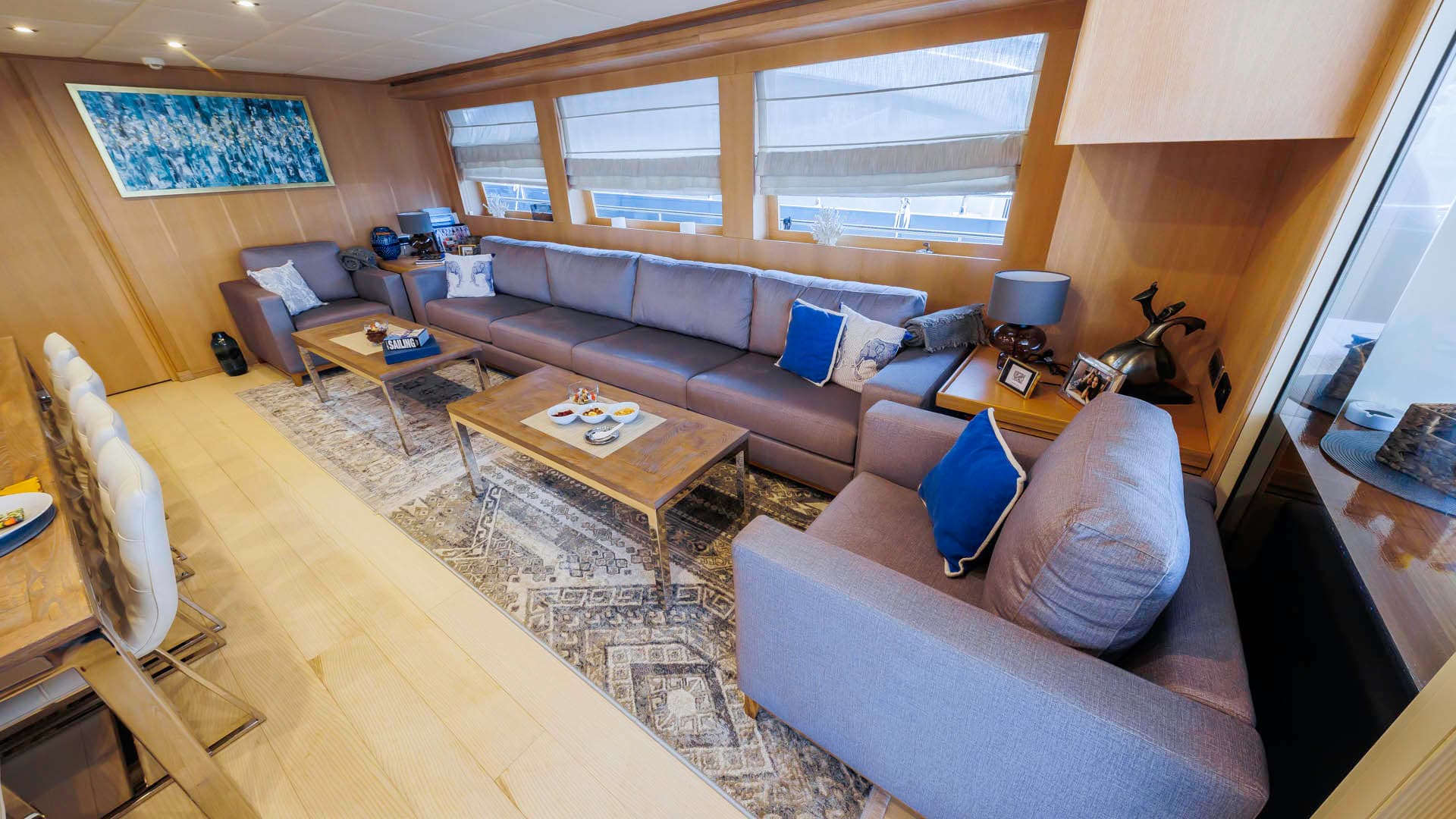 Yacht salon interior with wood paneling, gray sectional sofa, and coffee table with snacks.