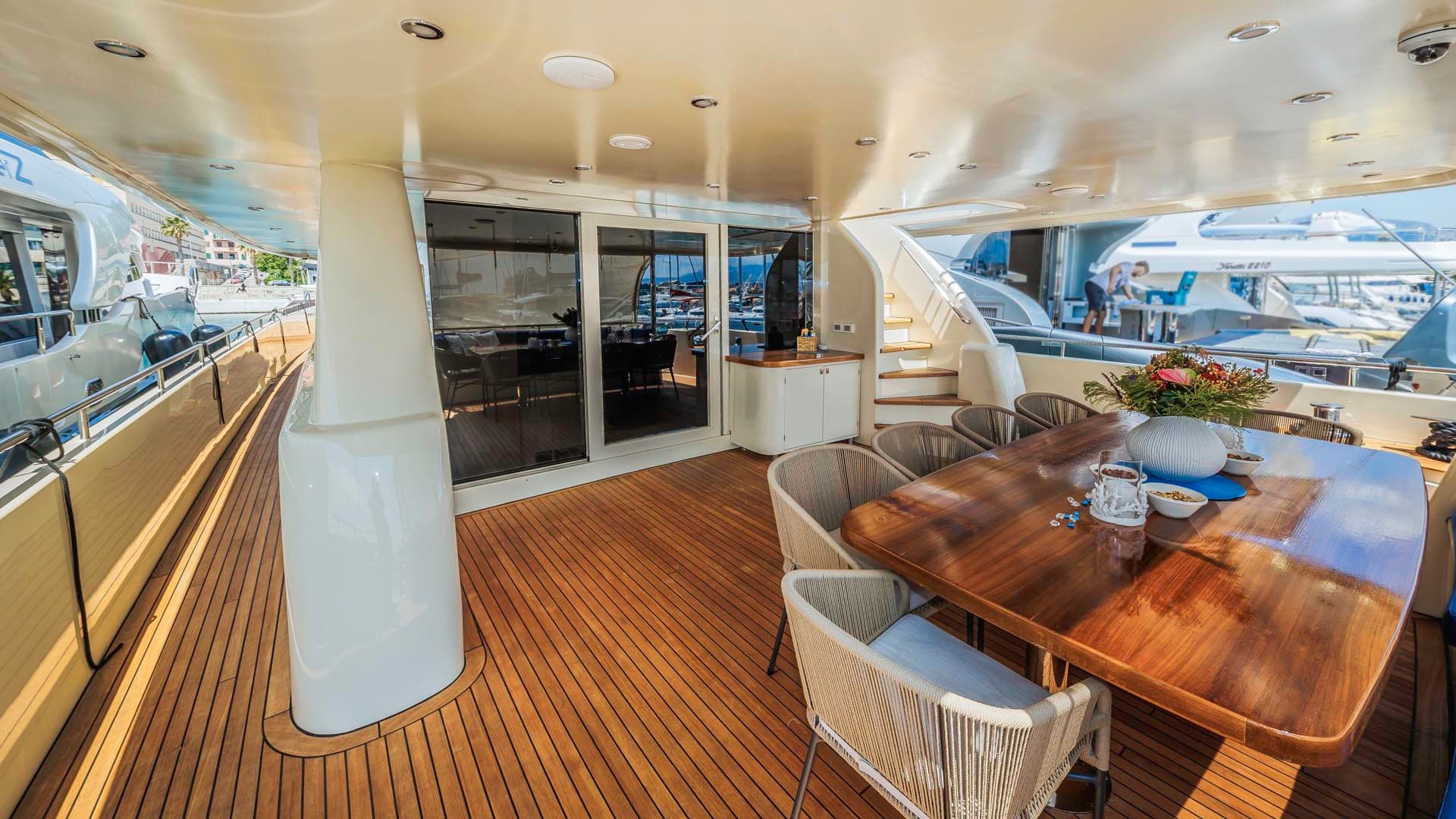 Outdoor dining area on a yacht with teak deck, wooden table, and harbor view