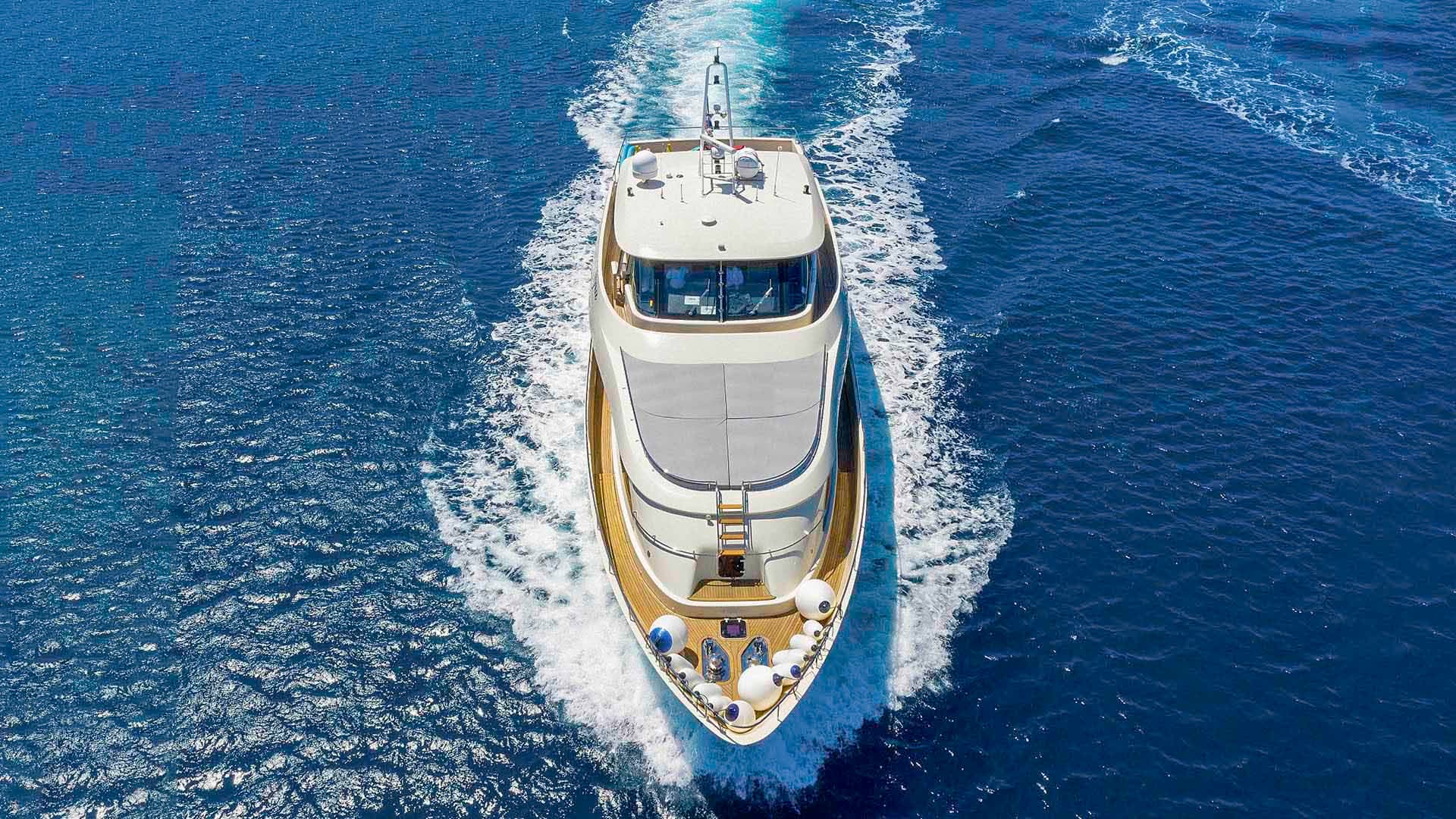 Motor yacht running at speed on deep blue coastal waters, seen from above.