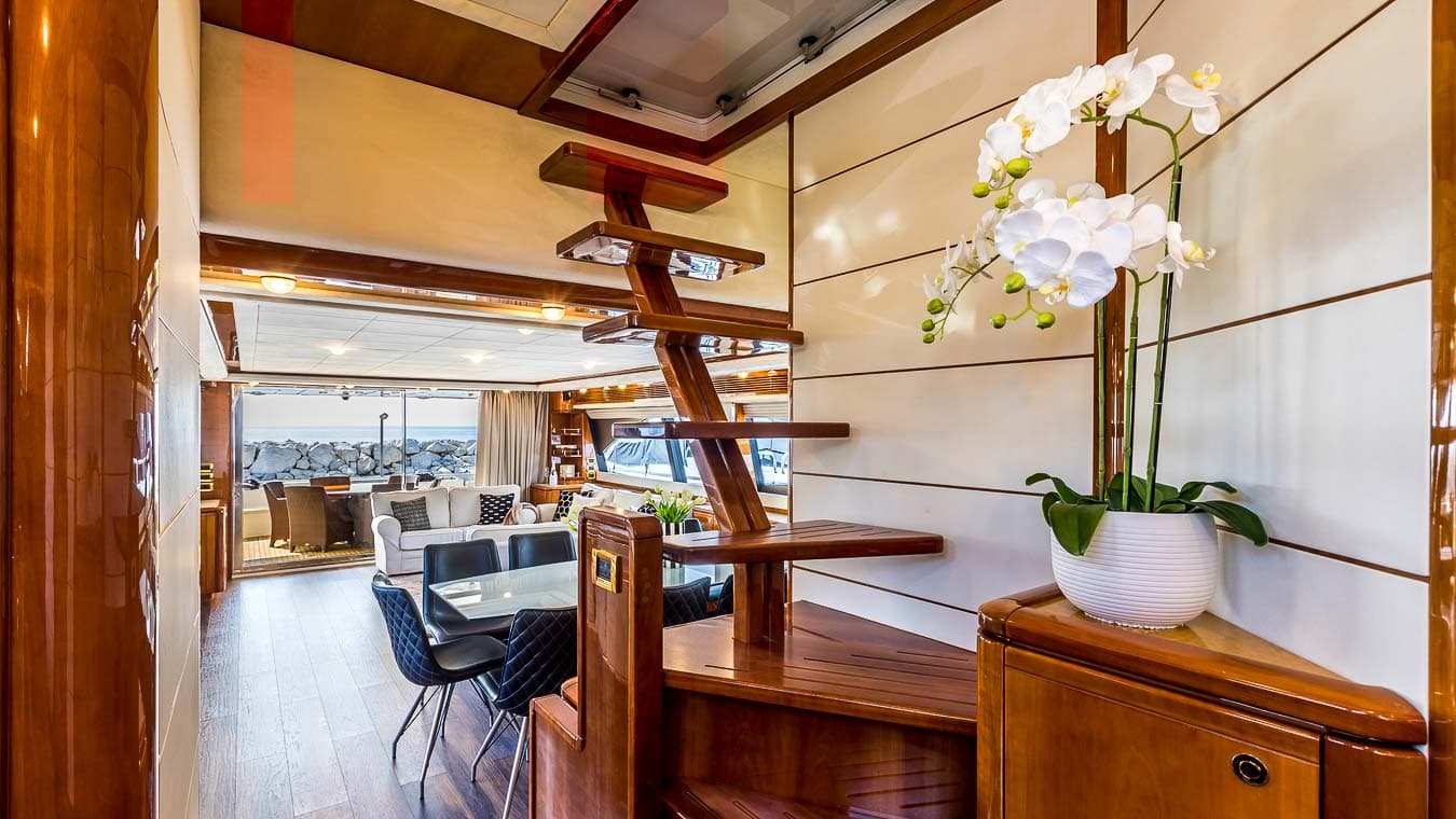 Wooden staircase to fly bridge inside luxury yacht with view of rocky sea wall